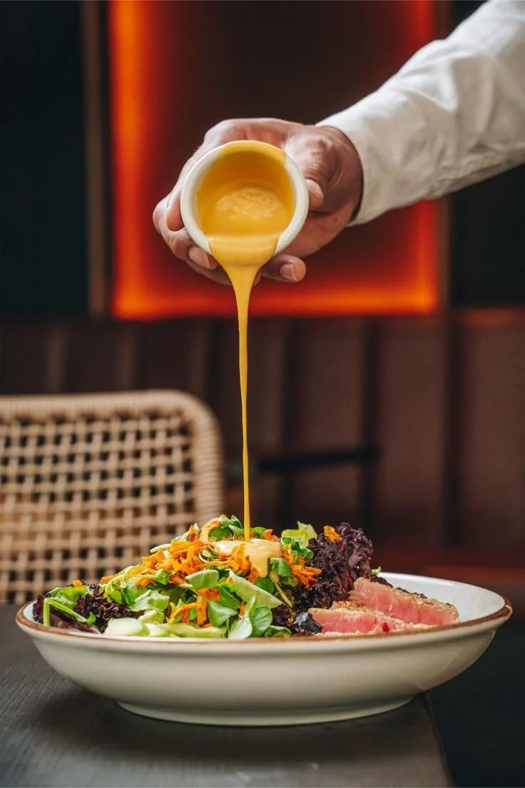 Persona sirviendo aderezo de mostaza en una ensalada con carne y verduras.