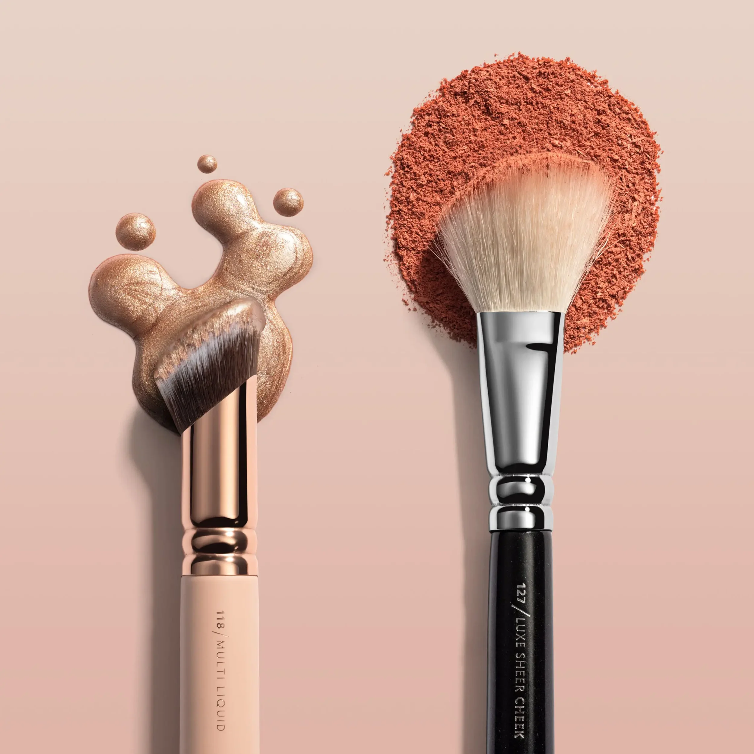 Brochas de maquillaje con diferentes estilos y colores, algunas con acabado metálico y otras en negro, colocadas en una superficie de color rosa claro.
