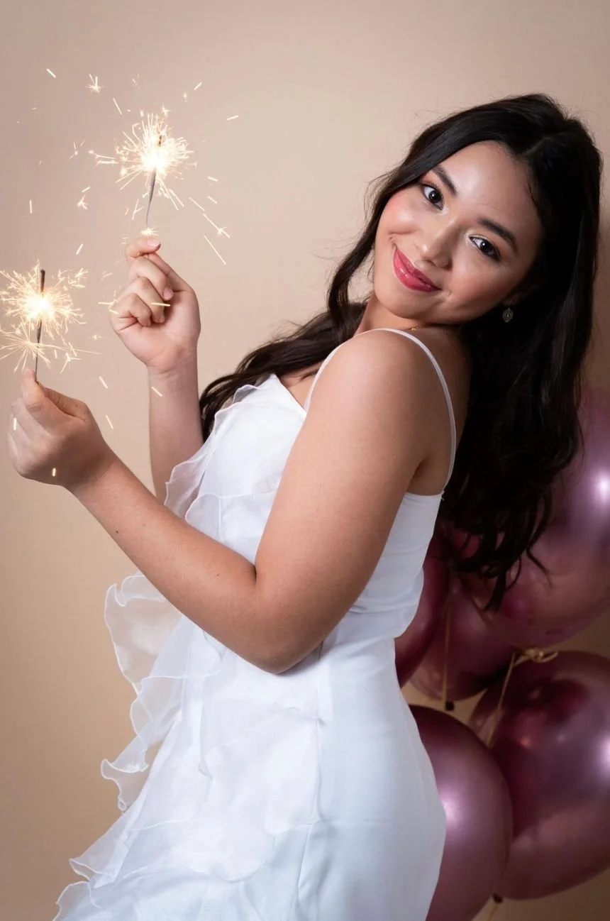Mujer sonriendo con globos y fuegos artificiales en las manos.