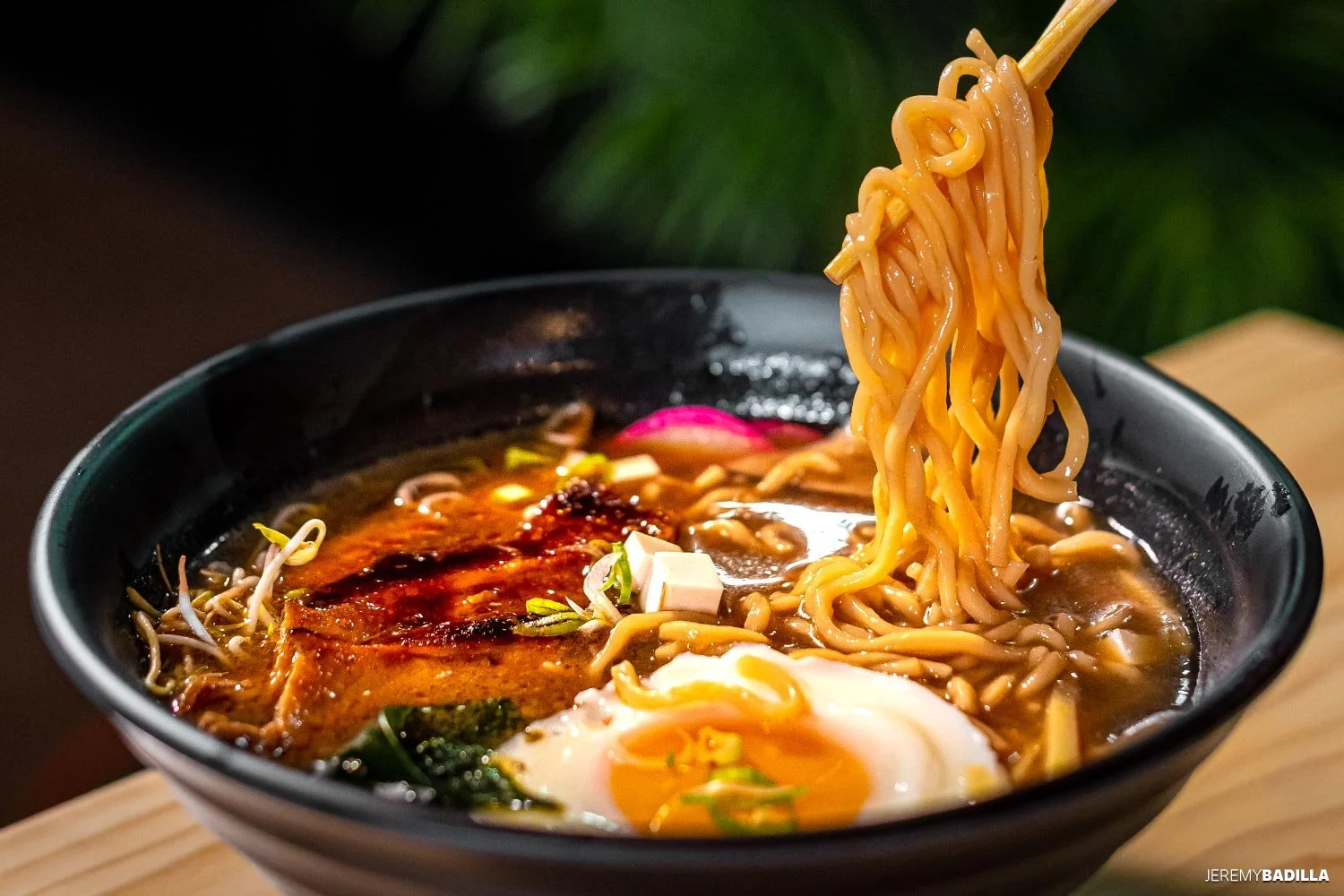 Un tazón con ramen, fideos amarillos, un huevo poche, vegetales, salsa y otros ingredientes en un caldo oscuro