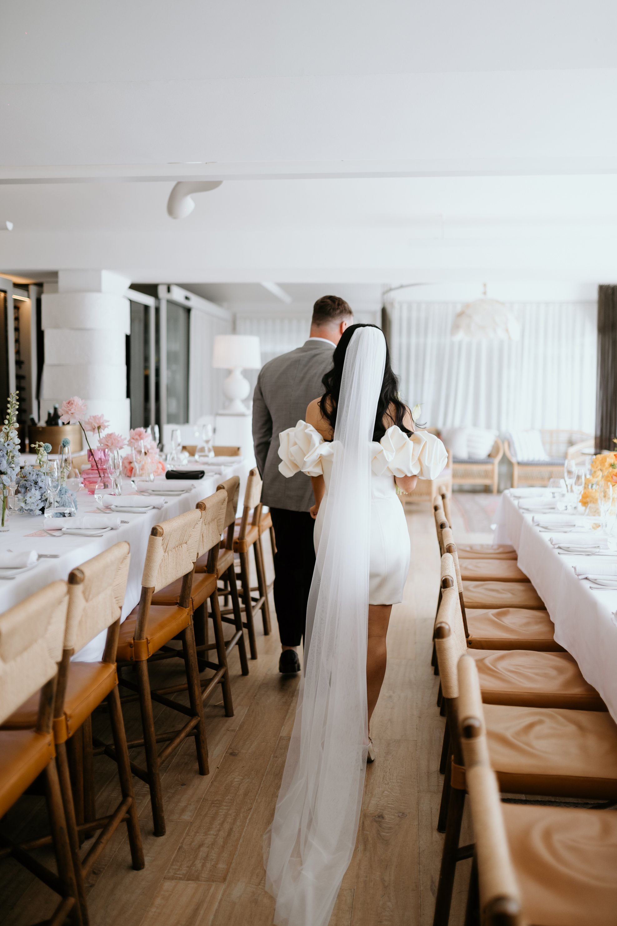 Bride and groom walk into a decorated dining area for a wedding reception.