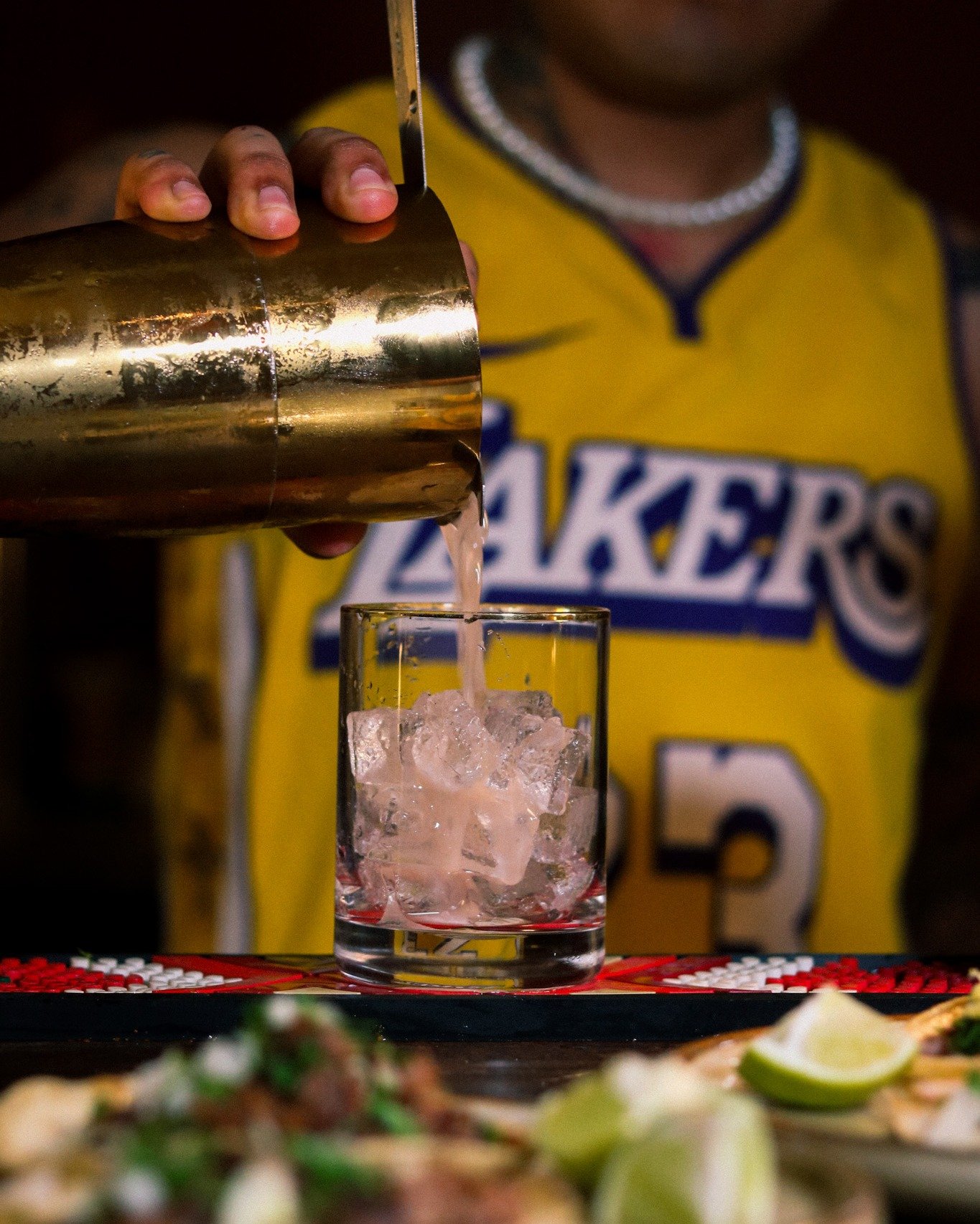 The pour is the moment.
Shaker tipped, ice catching the strain, fresh juice landing where it should.
No bottles with measured pumps, no shortcuts behind the wood.
Tacos waiting below, drink coming together above &mdash; this is how a night gets built