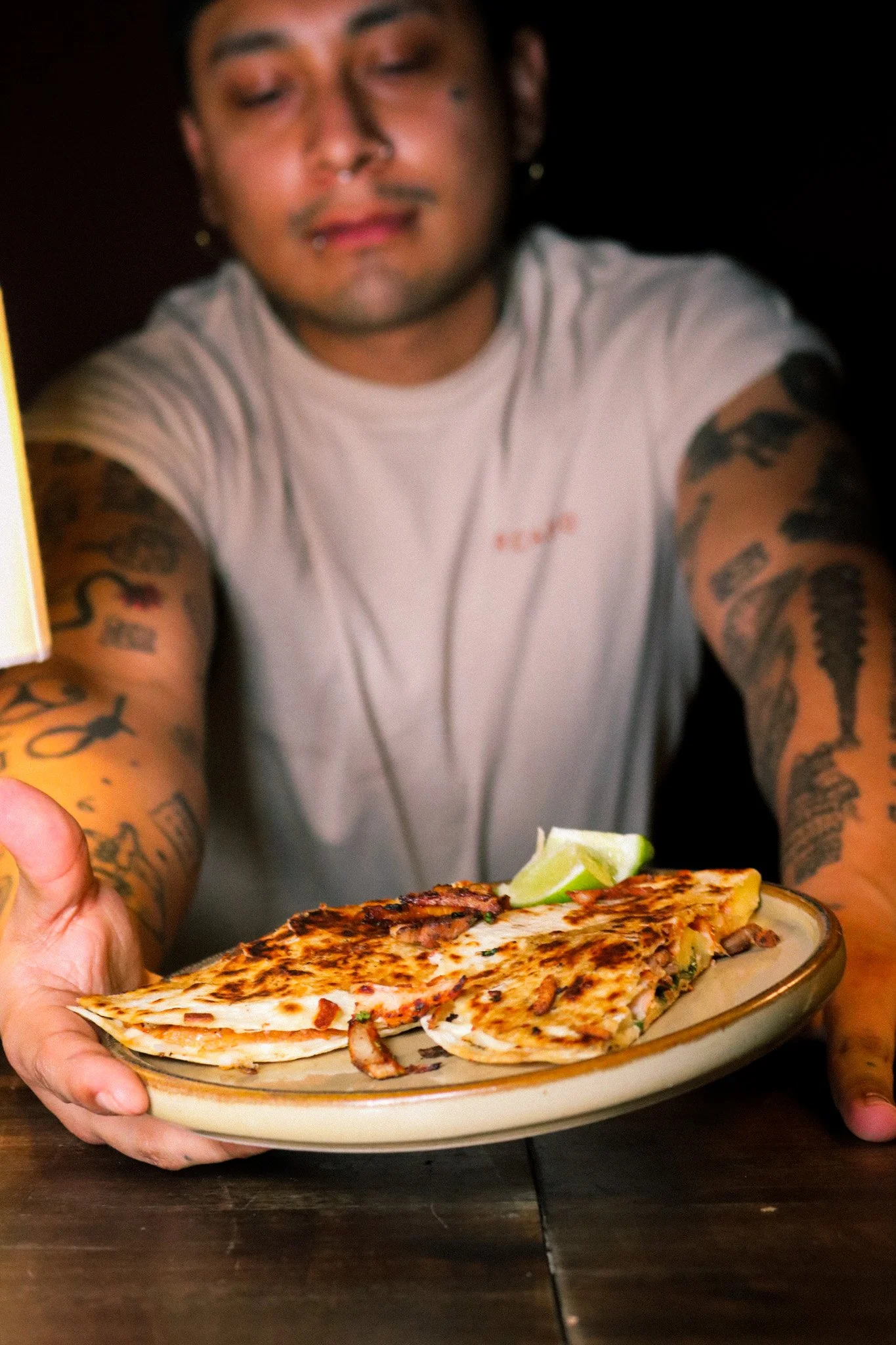 Person extending a plate of two slices of grilled quesadillas with a lime wedge on top.