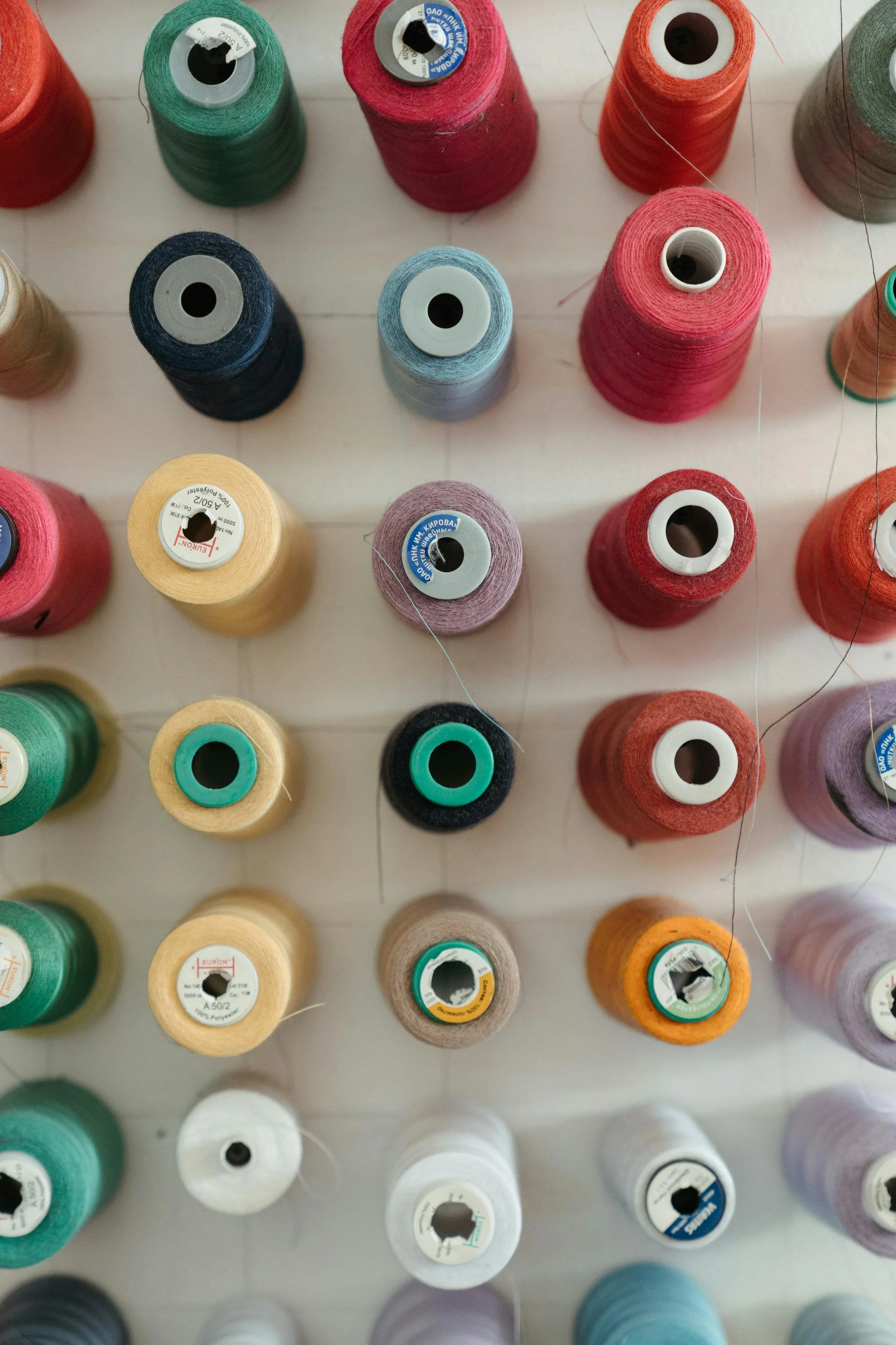 Conos de diferentes colores de hilo de coser y bordar en un patrón organizado sobre una superficie clara.