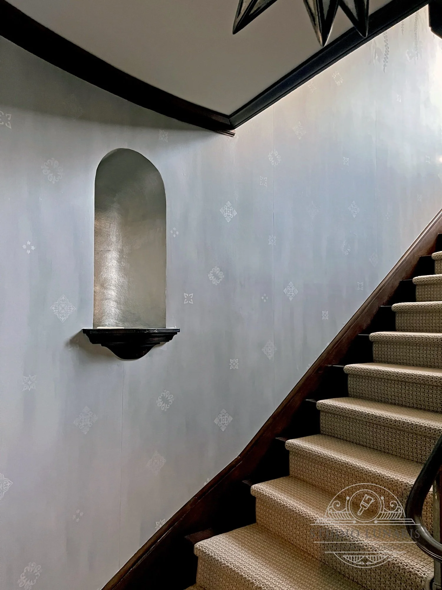 Stairwell ornamental stencil pattern on a softly painted gray background.