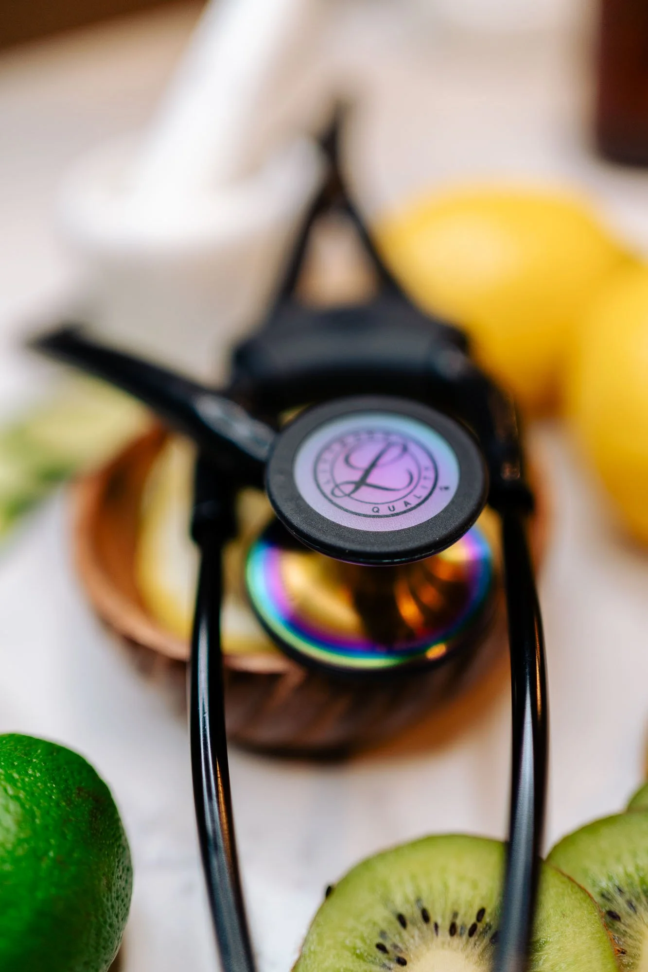 A close-up of rainbow-colored sunglasses with a logo on the lens, surrounded by kiwifruit slices and limes on a white surface.