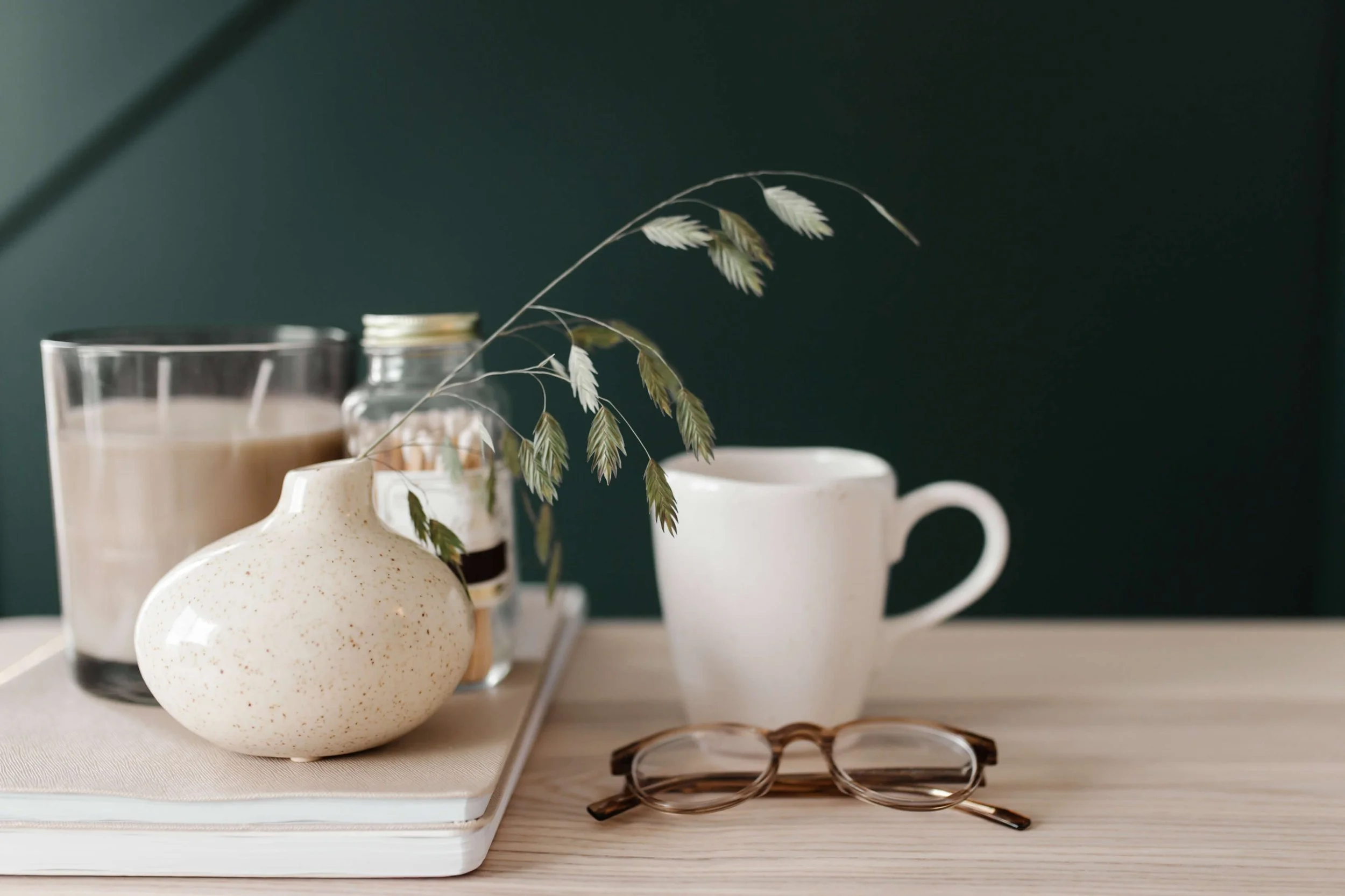 glasses coffee mug and candle on desk by green wall