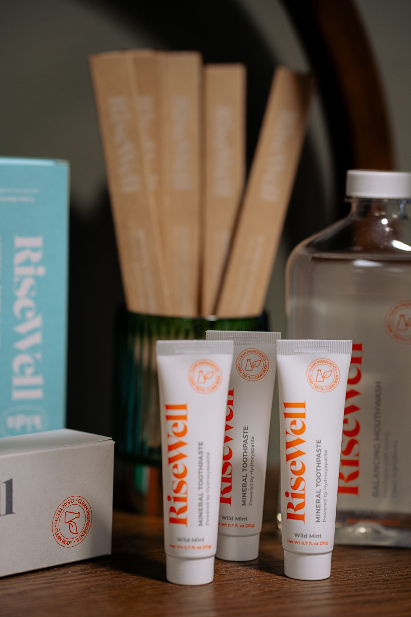 Four tubes of RiseUse mineral toothpaste with wild mint flavor placed on a wooden surface, with a bottle and partially visible box in the background.