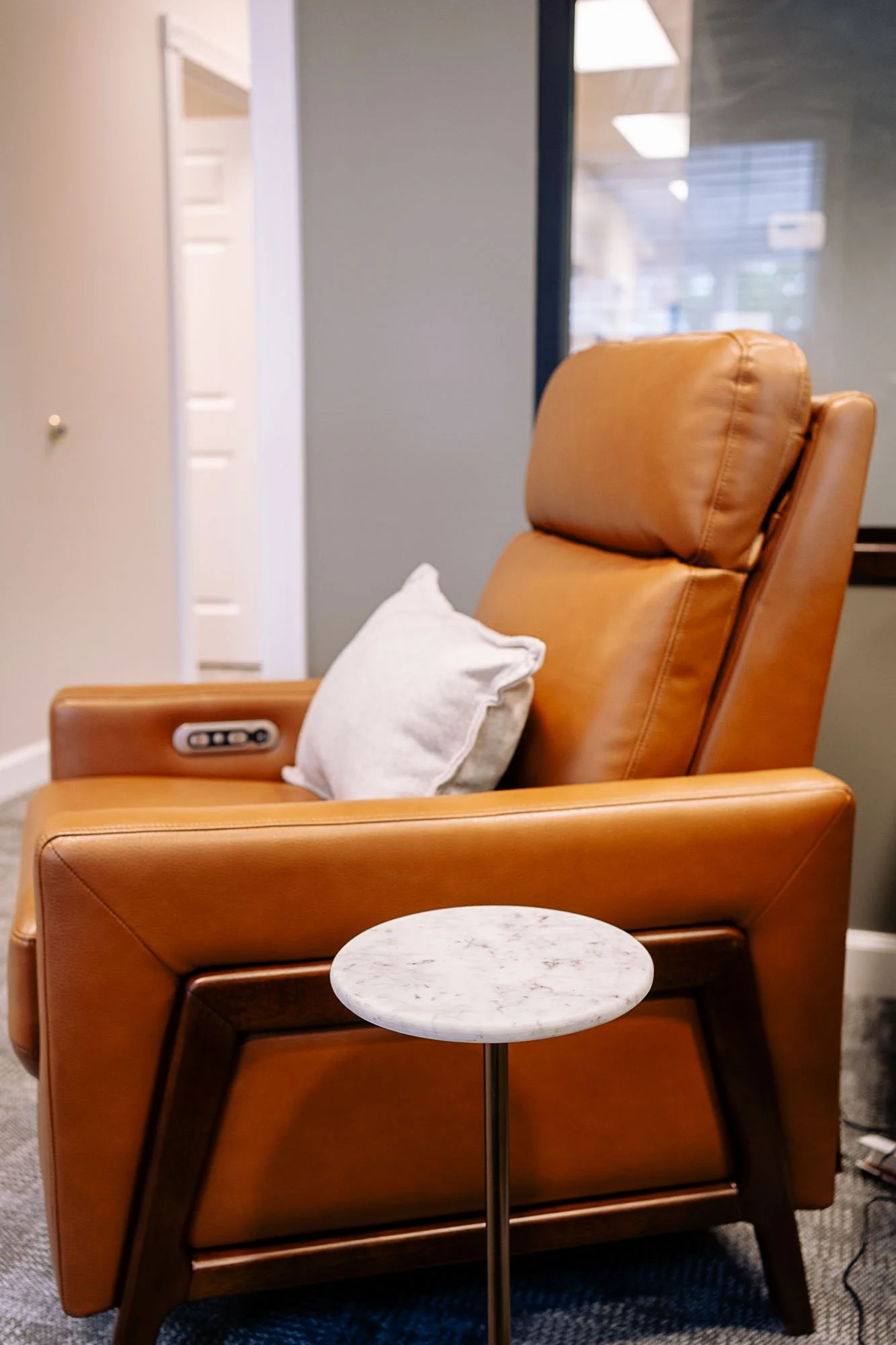 An orange leather chair with a white pillow on it next to a small round marble-top side table in a modern indoor setting.