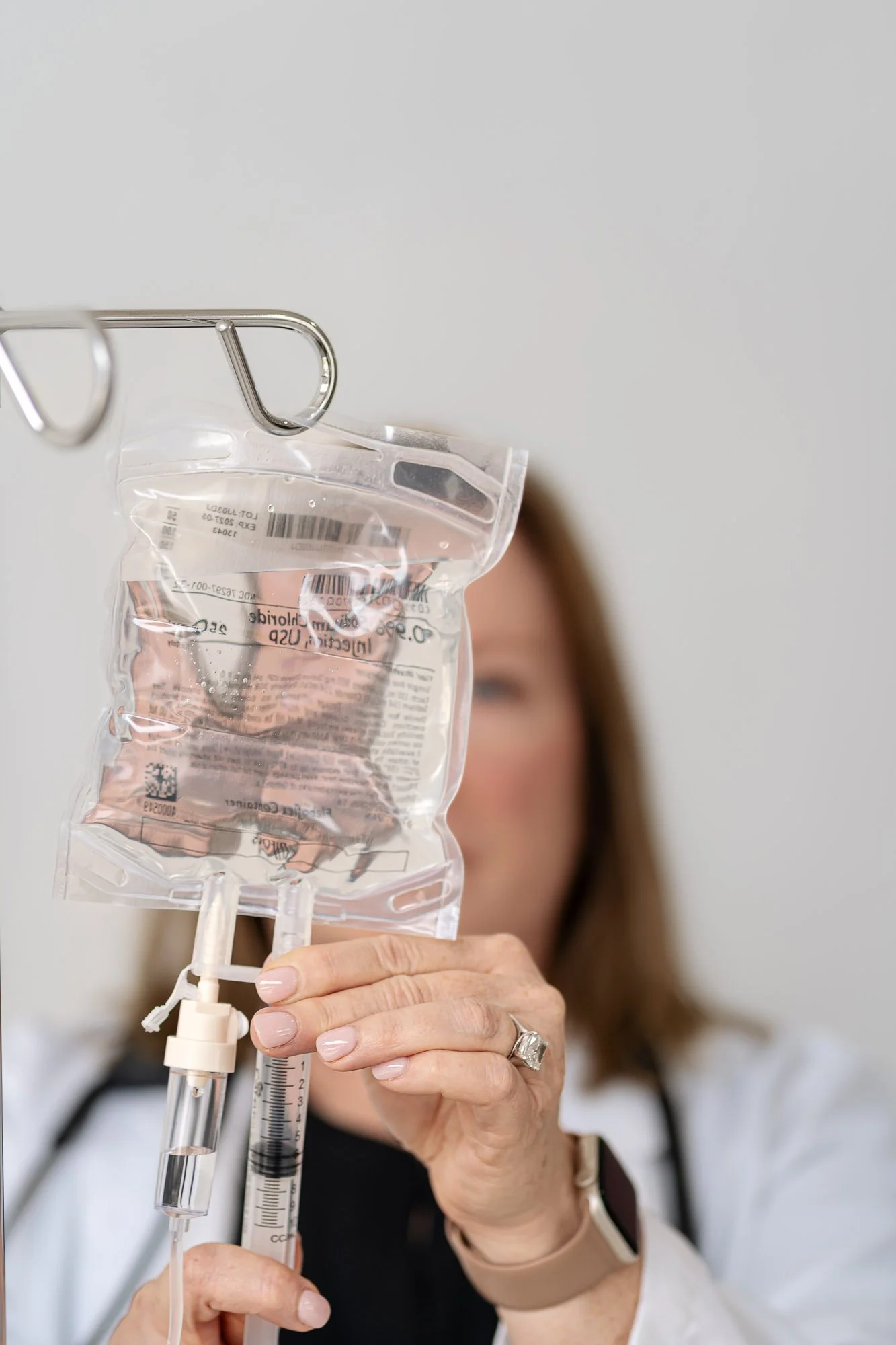 A healthcare professional is preparing intravenous fluids with a sterile IV bag and syringes in a medical setting.