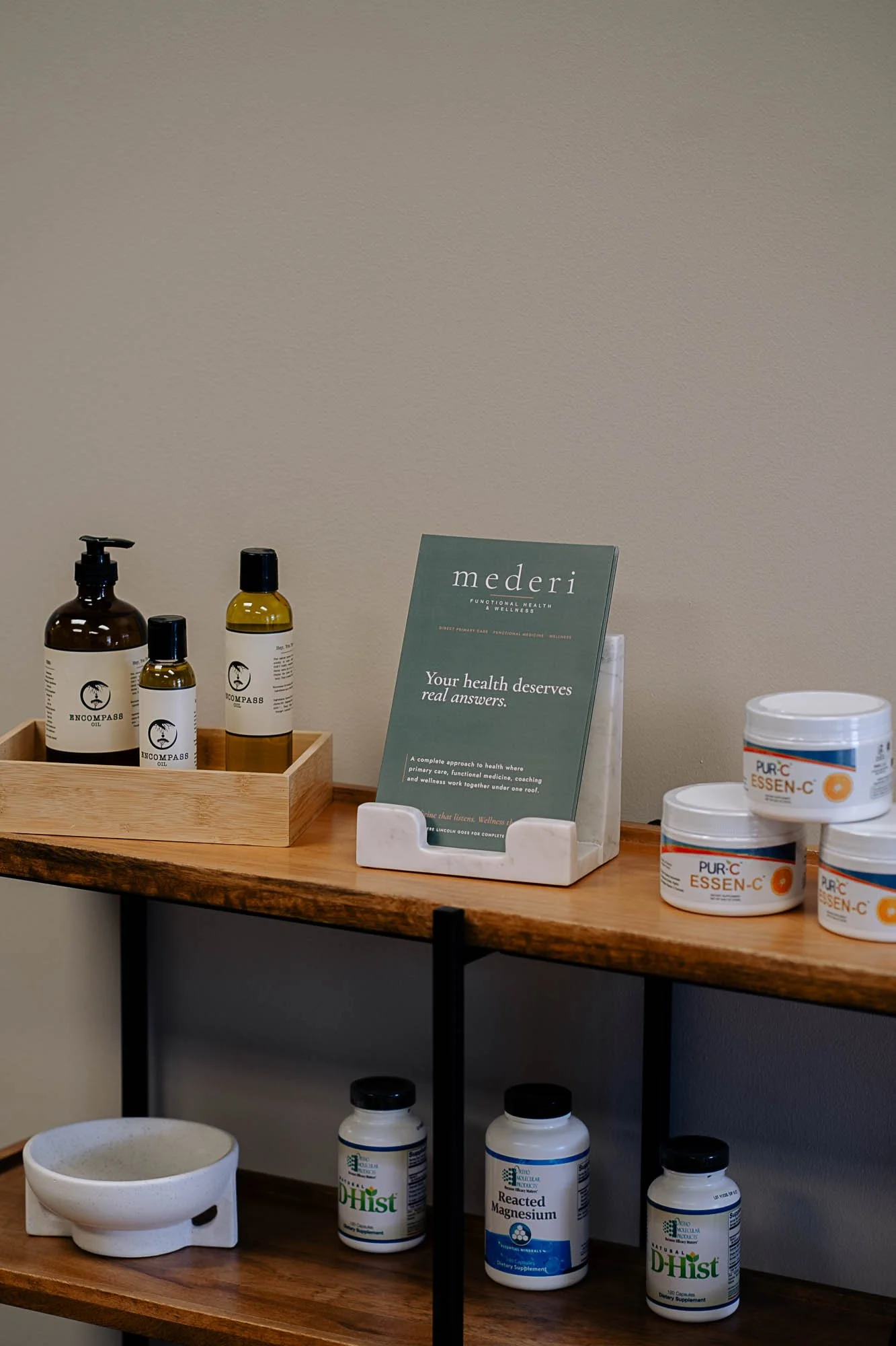 Display of health and wellness products including bottles of essential oils, dietary supplements, and informational brochures on a wooden shelf.