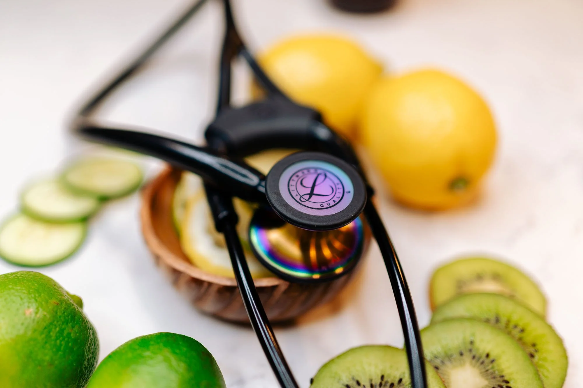 Sunglasses and a stethoscope on a white surface with fresh green limes and sliced kiwifruit