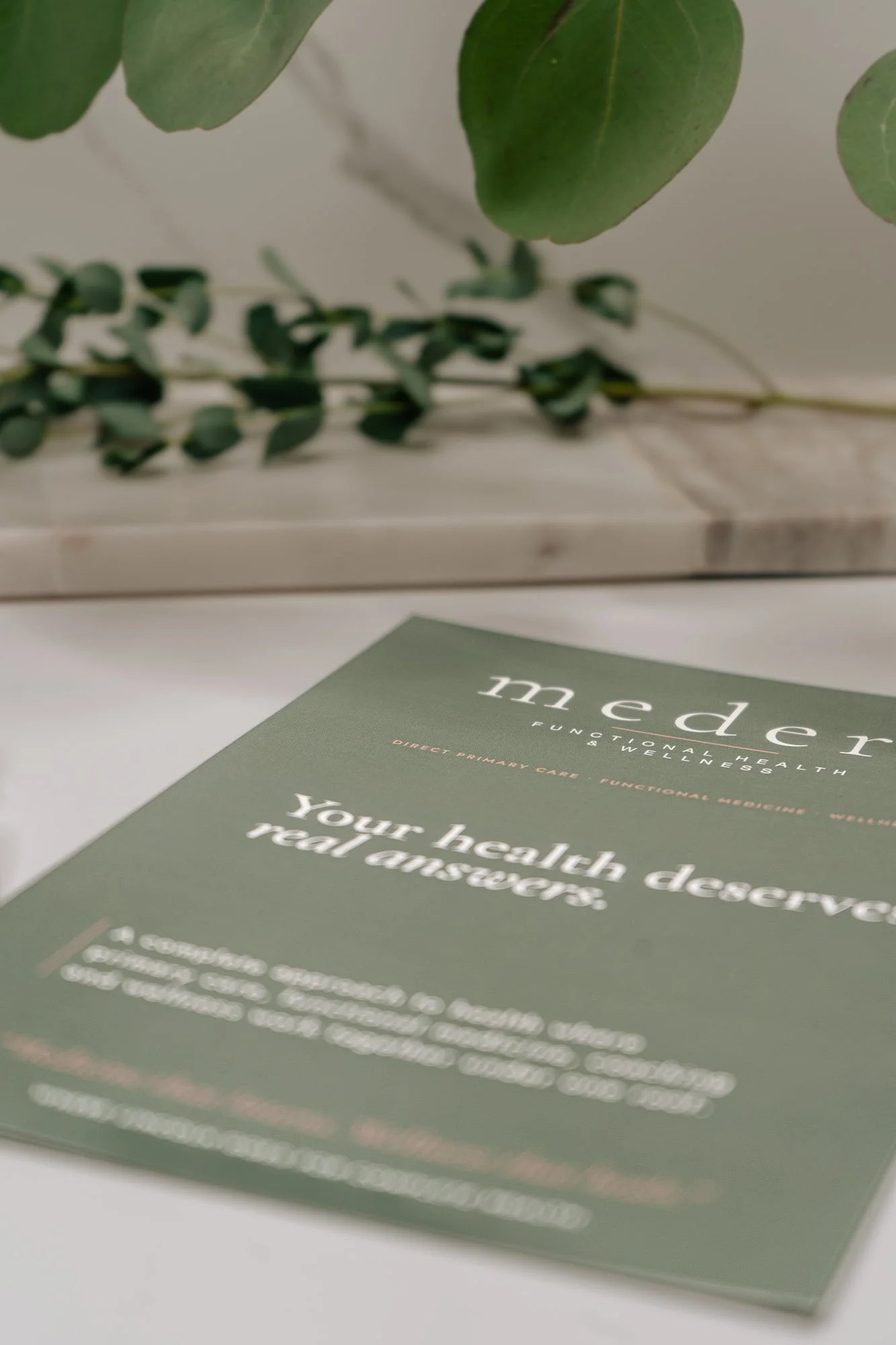 A brochure on a table with green background and white text about healthcare services, with a plant in the background.