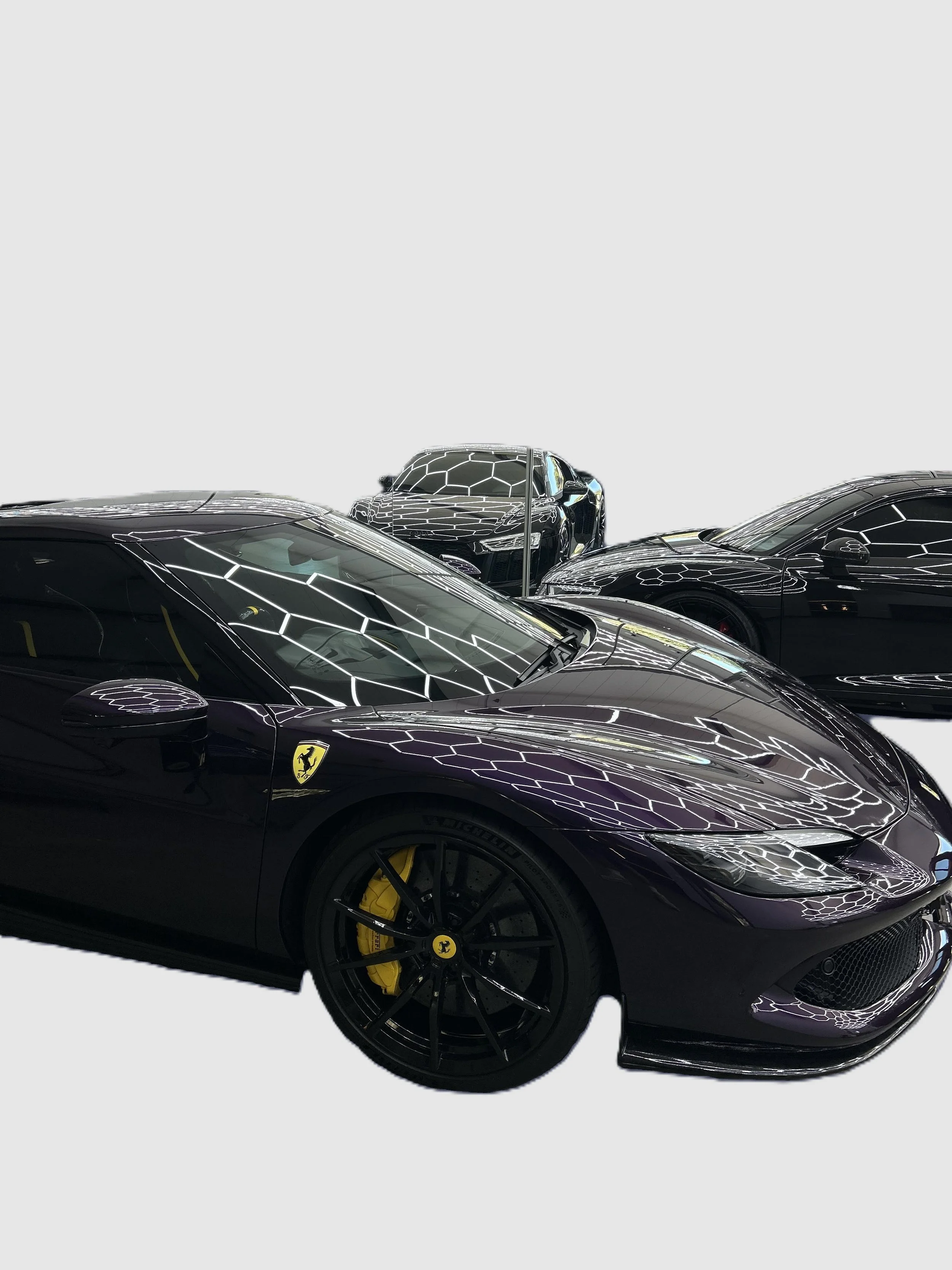 Black Ferrari sports car with yellow brake calipers in a showroom, with reflections of ceiling lights on the hood and roof, alongside other luxury cars.