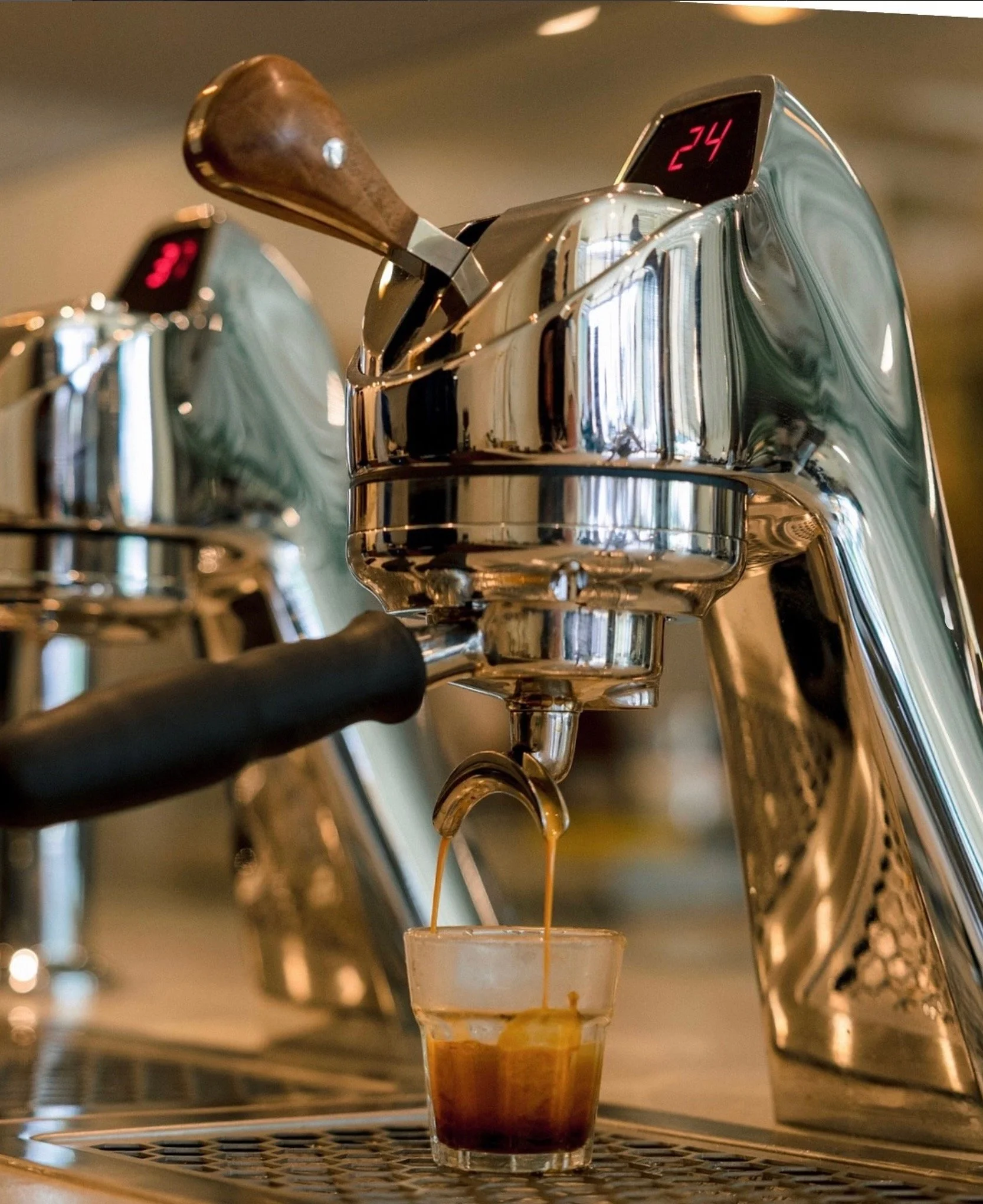 Close-up of a silver espresso machine pouring coffee into a glass cup with lemon slices at the base and a digital display showing the number 24.