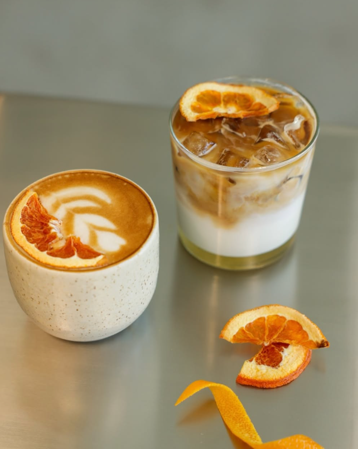 Close-up of two orange and vanilla drinks with orange slices on a metallic surface.