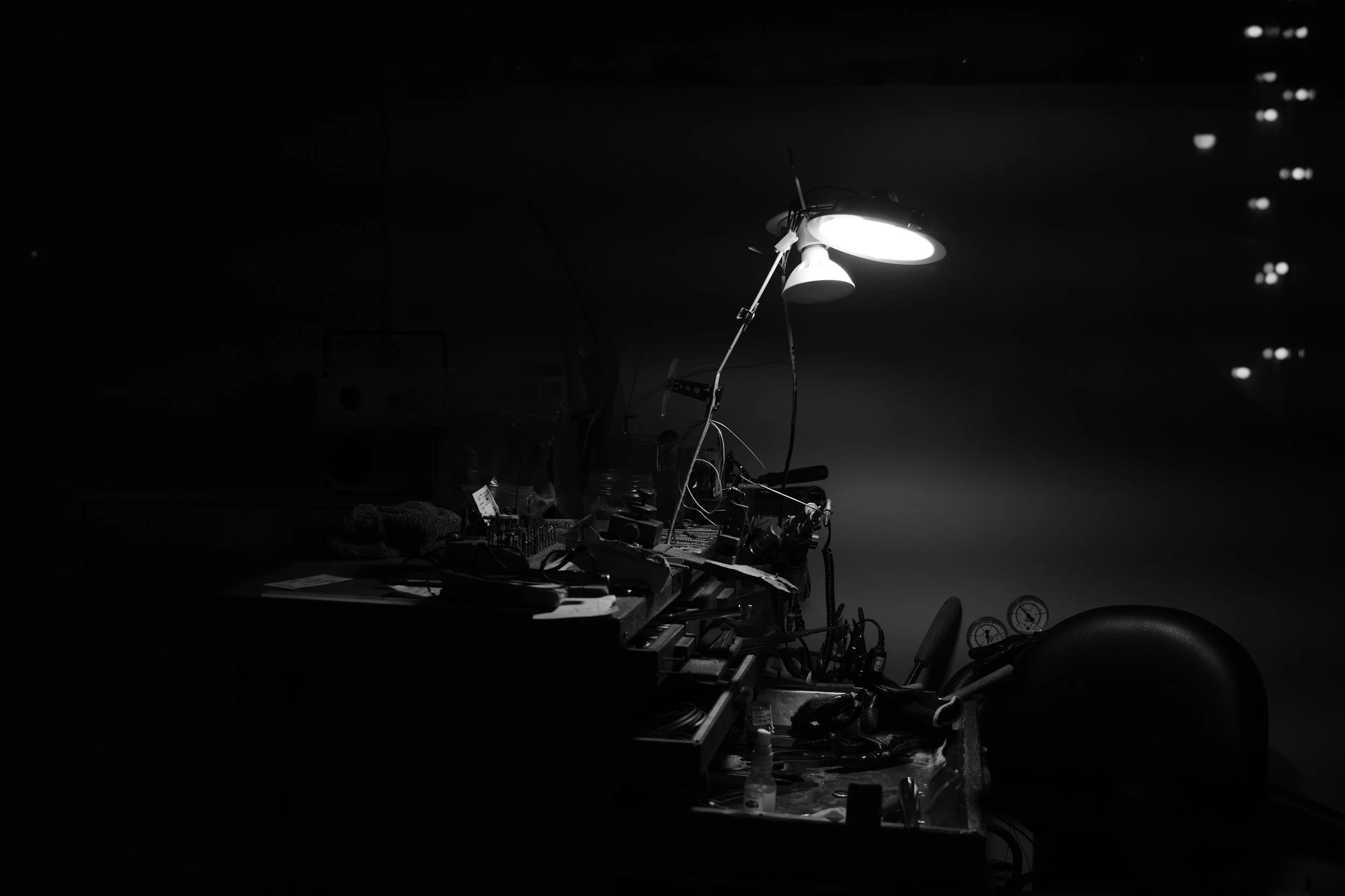 Black and white atmospheric photo of a jeweler's workbench illuminated by a single task lamp.