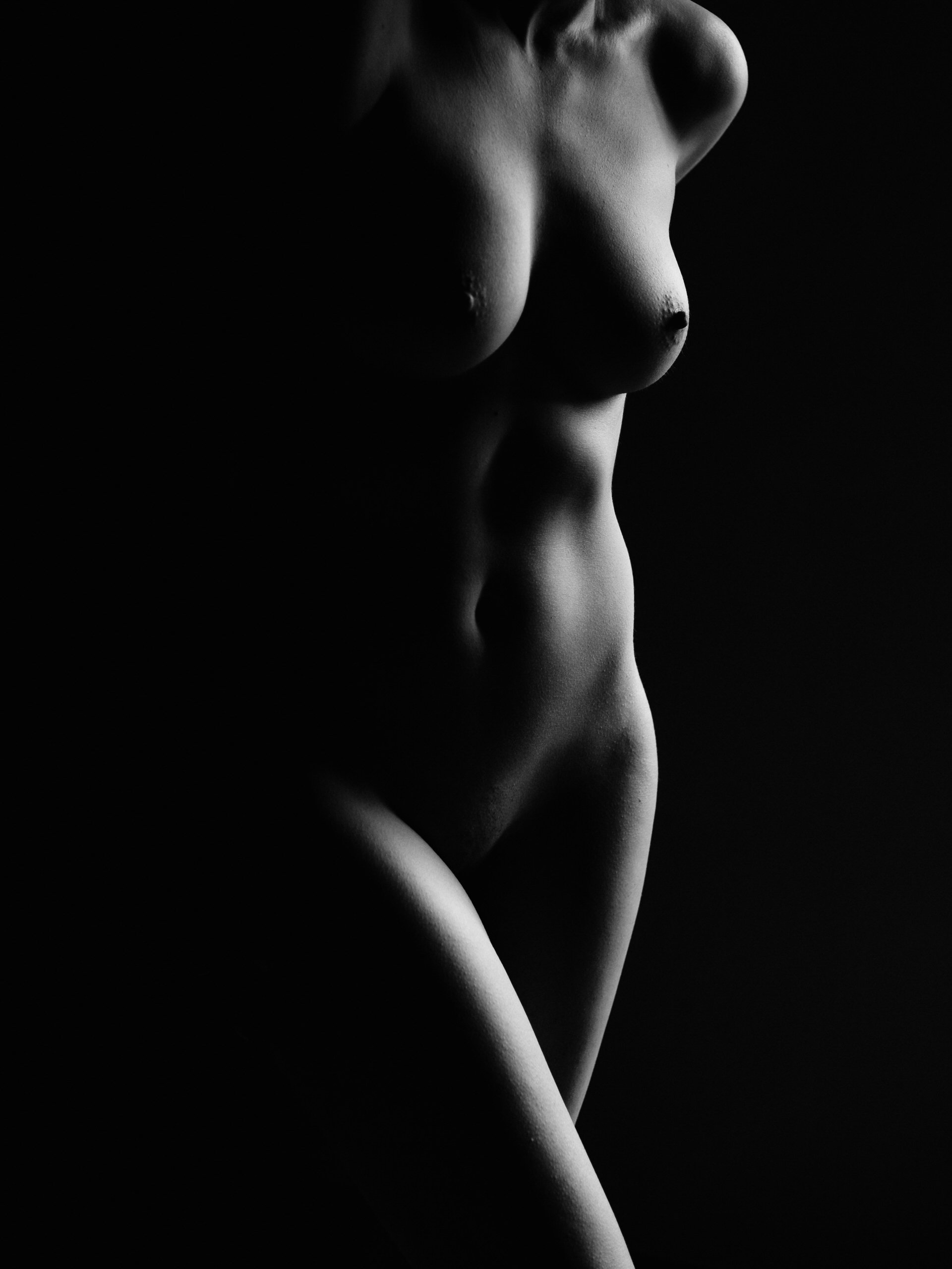 Corps d'une femme nue en noir et blanc, partiellement éclairé, avec un fond noir.