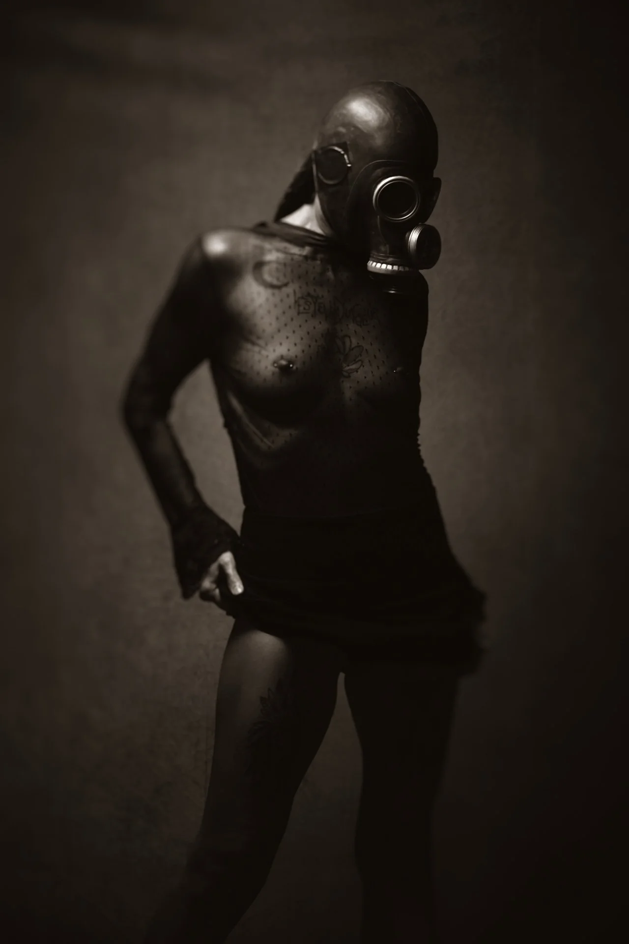 Une personne portant un masque à gaz et vêtue de vêtements noirs, debout dans un décor sombre.