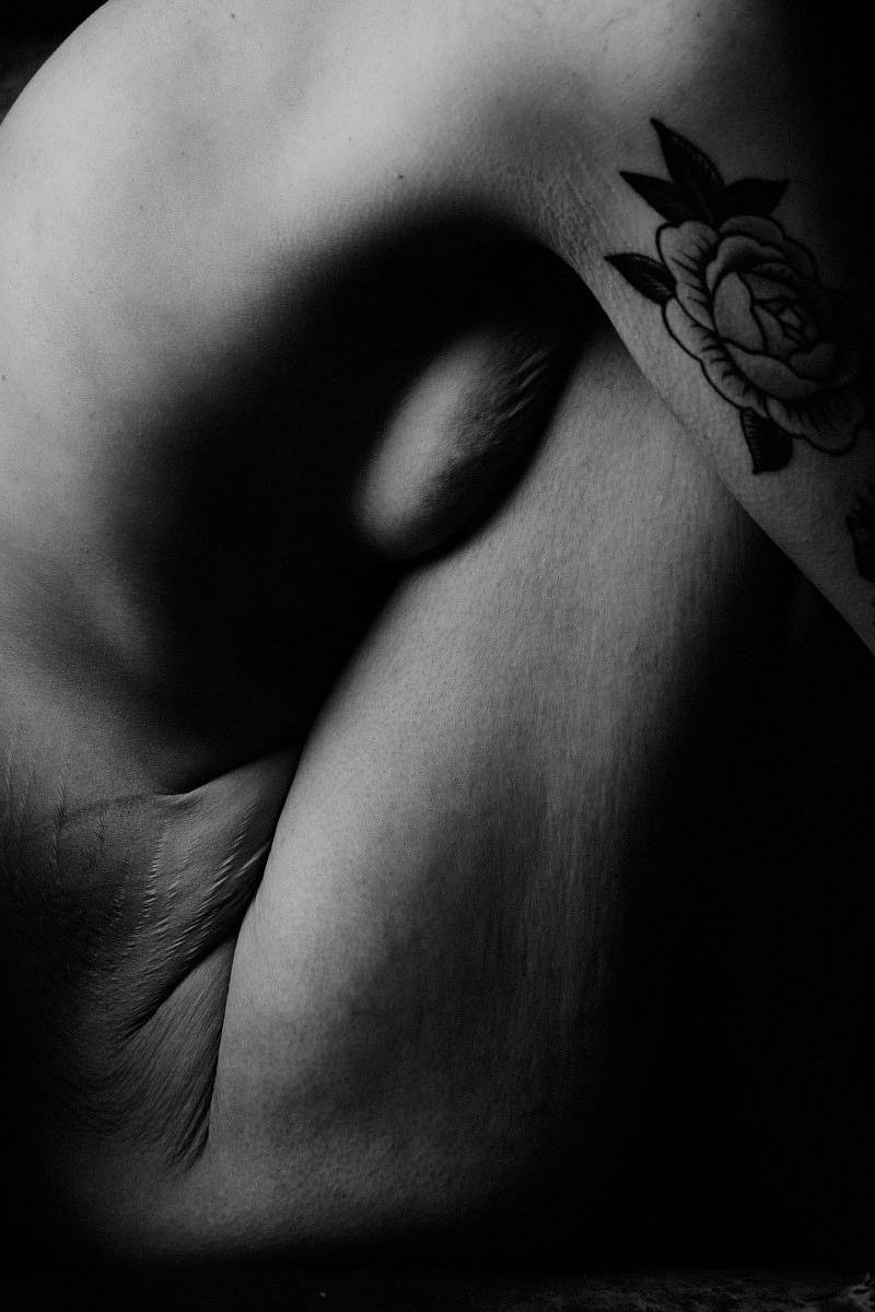 Une photographie en noir et blanc représentant une partie du corps d'une personne, apparemment une poitrine avec un tatouage de rose sur l'épaule.