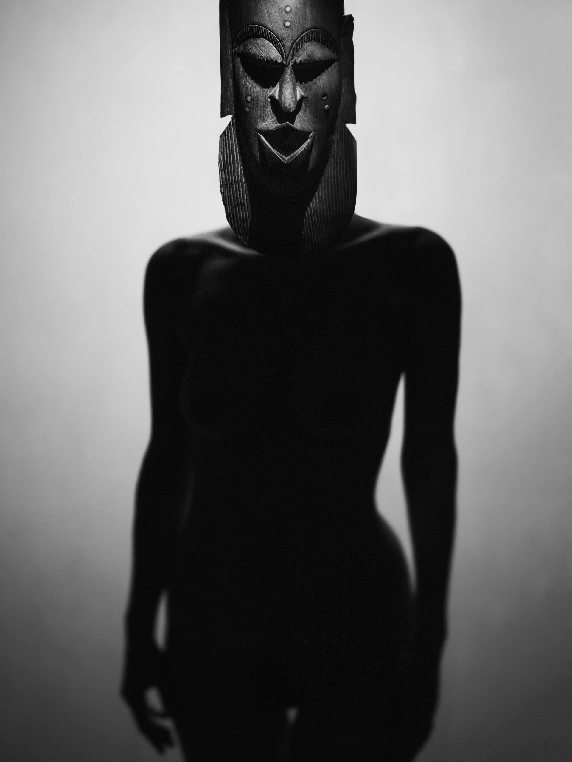 Une silhouette de femme nue portant un masque africain en bois, en noir et blanc.