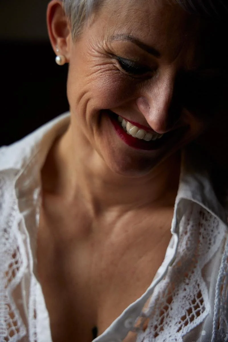 Femme souriante avec des bijoux en perles et vêtue d'une chemise en dentelle blanche.