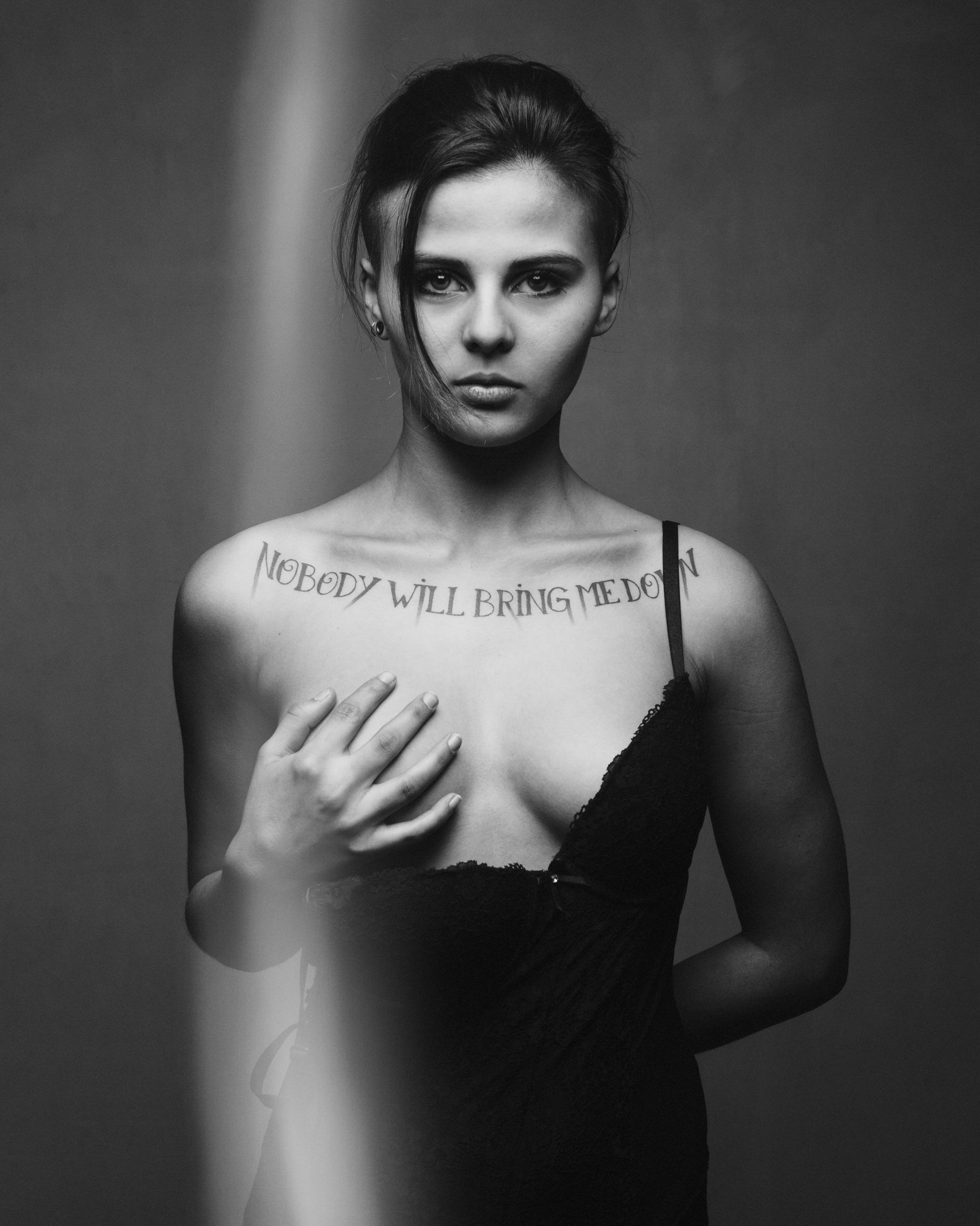 Jeune femme avec tatouage sur la poitrine disant 'Nobody will bring me down', portant une robe noire, regardant l'objectif.