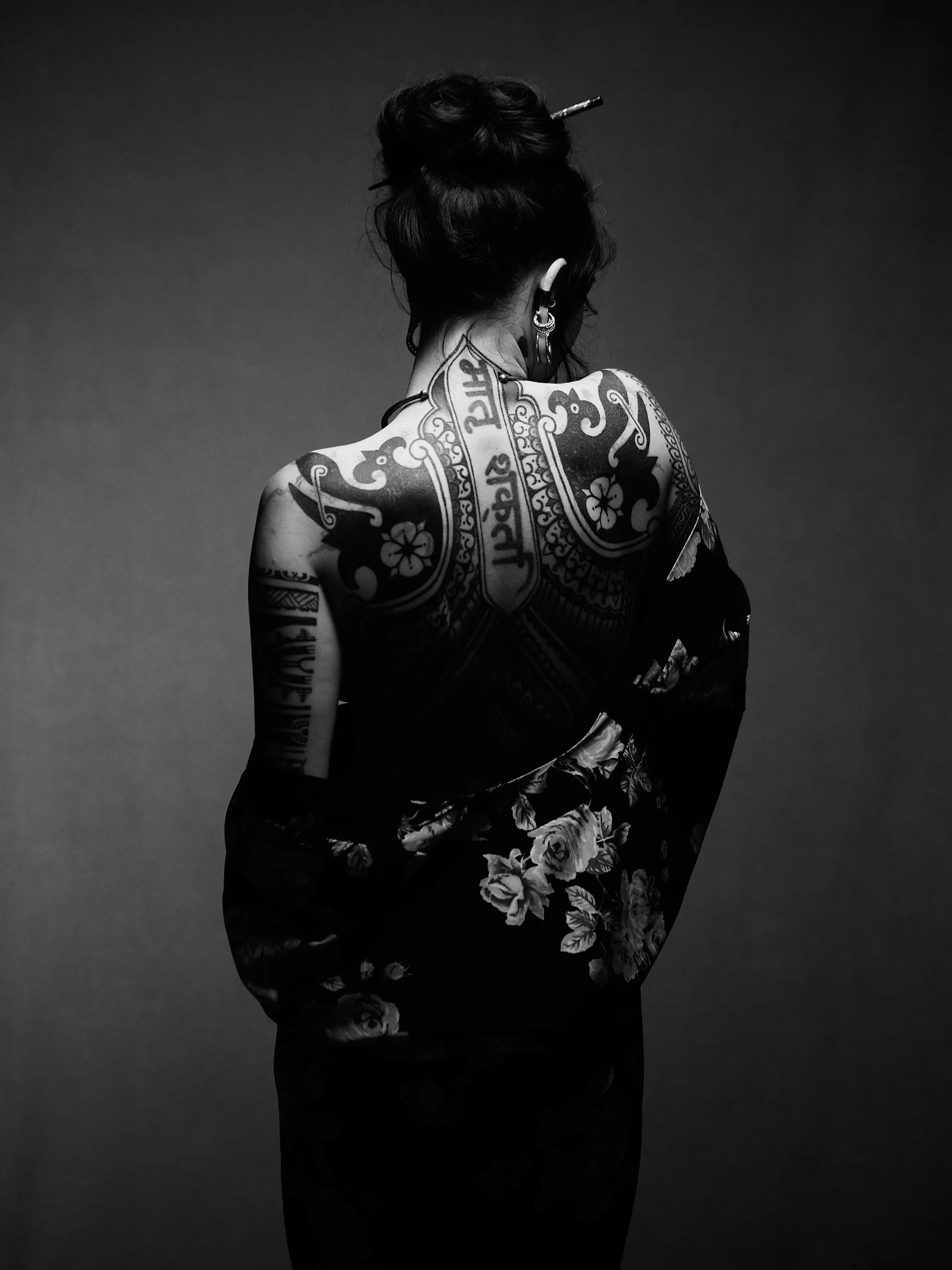 Une femme vue de dos avec des tatouages traditionnels sur le dos, portant une robe à fleurs et ayant les cheveux relevés avec un chignon.