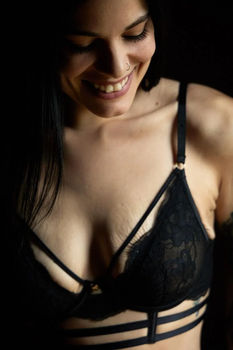 Une femme souriante portant un soutien-gorge en dentelle noire avec des lanières décoratives.