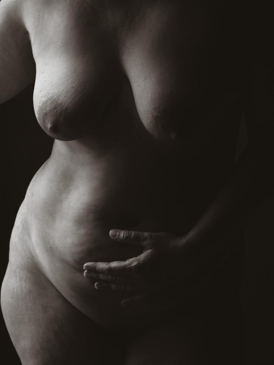 Statue de une femme nue, avec une main posée sur le ventre, en éclairage tamisé.