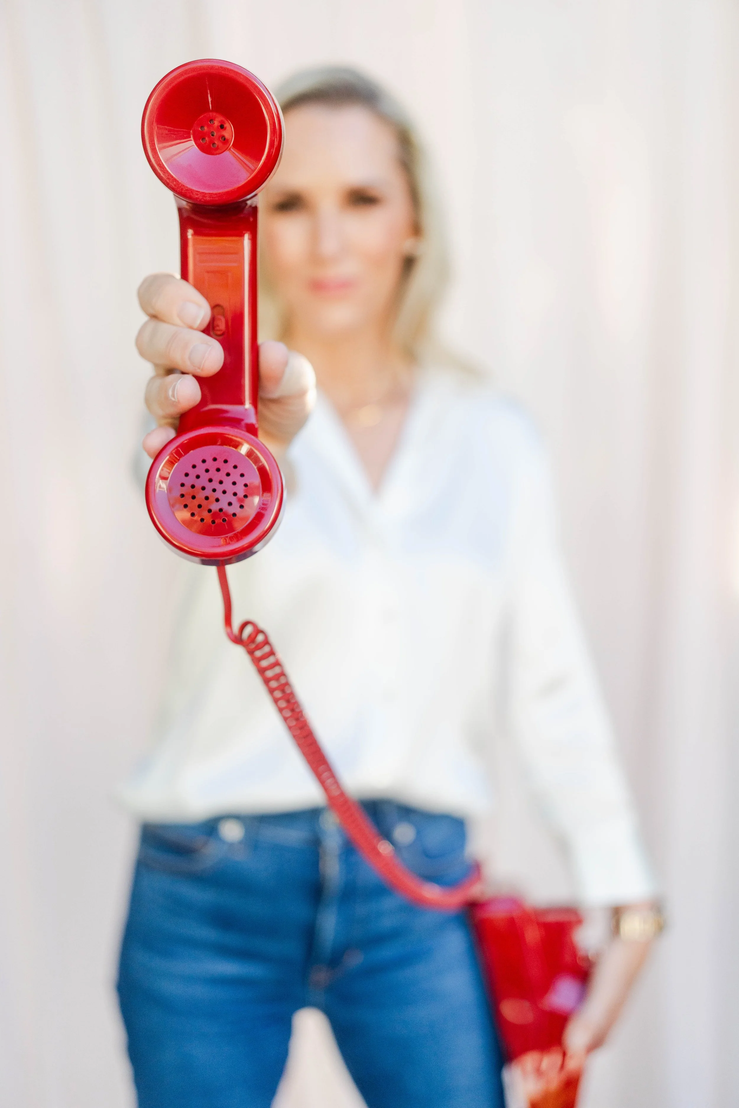 A woman is holding out a red telephone receiver towards the camera, with her face blurred in the background.