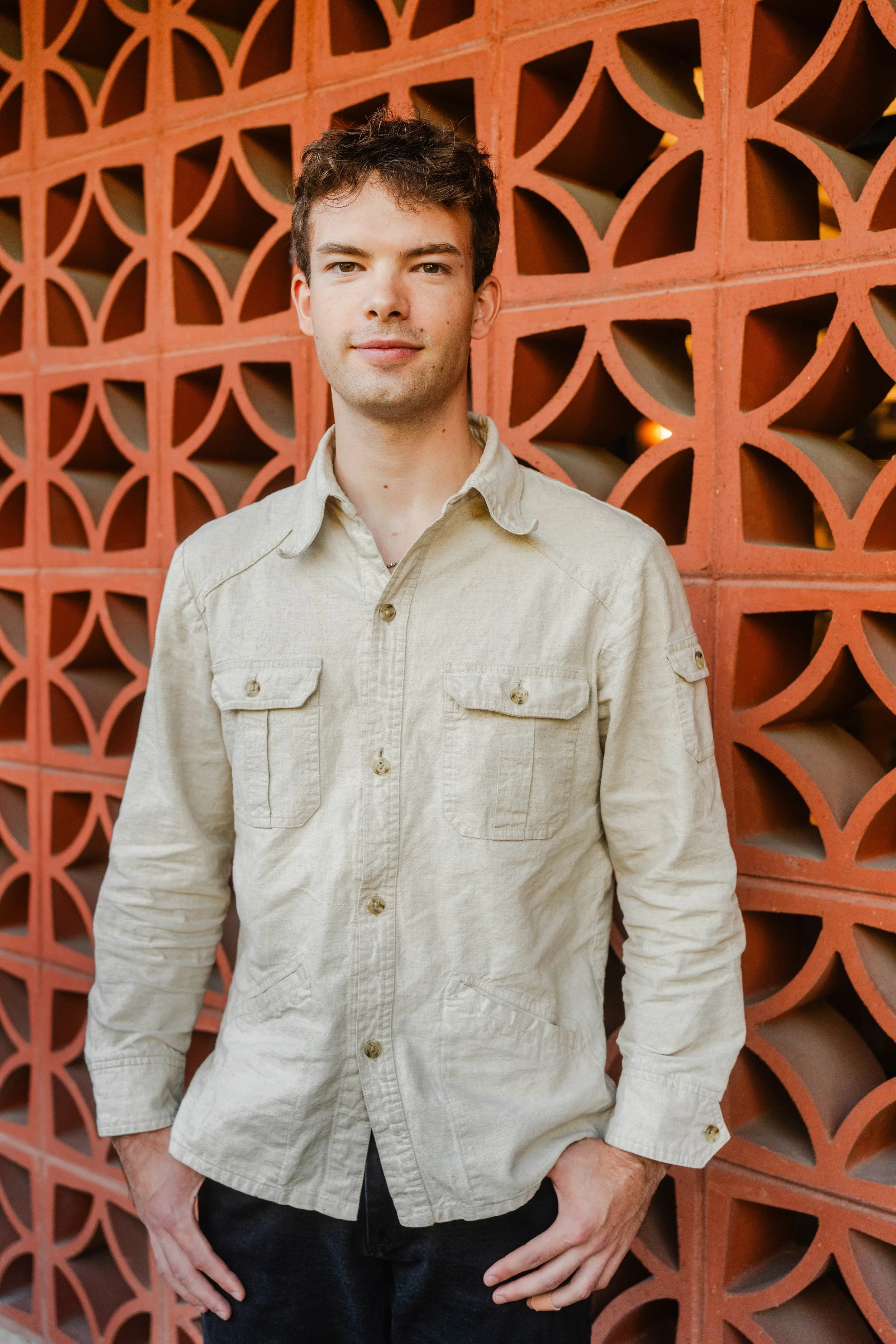 A young man standing with hands in pockets in front of a red decorative brick wall.