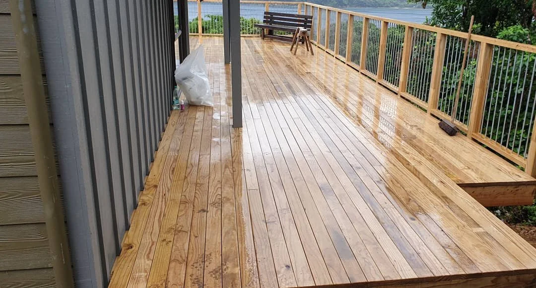 Wet wooden deck with a bench and scenic view of water and trees in the background.