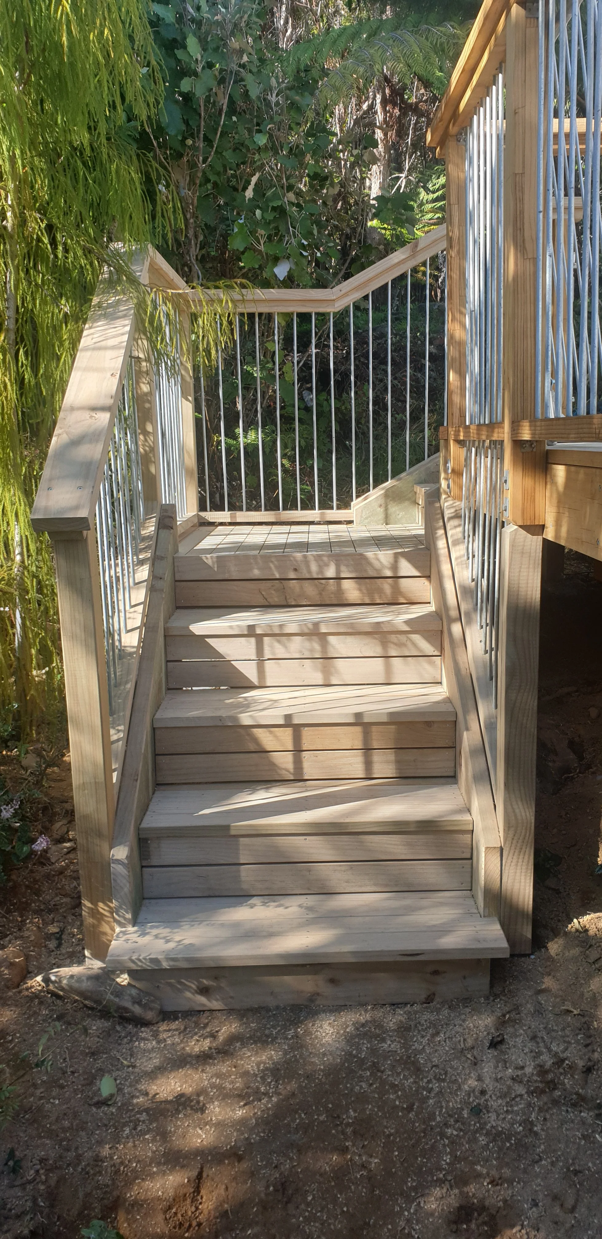 Wooden staircase with metal railings leading up to an elevated platform surrounded by green foliage.