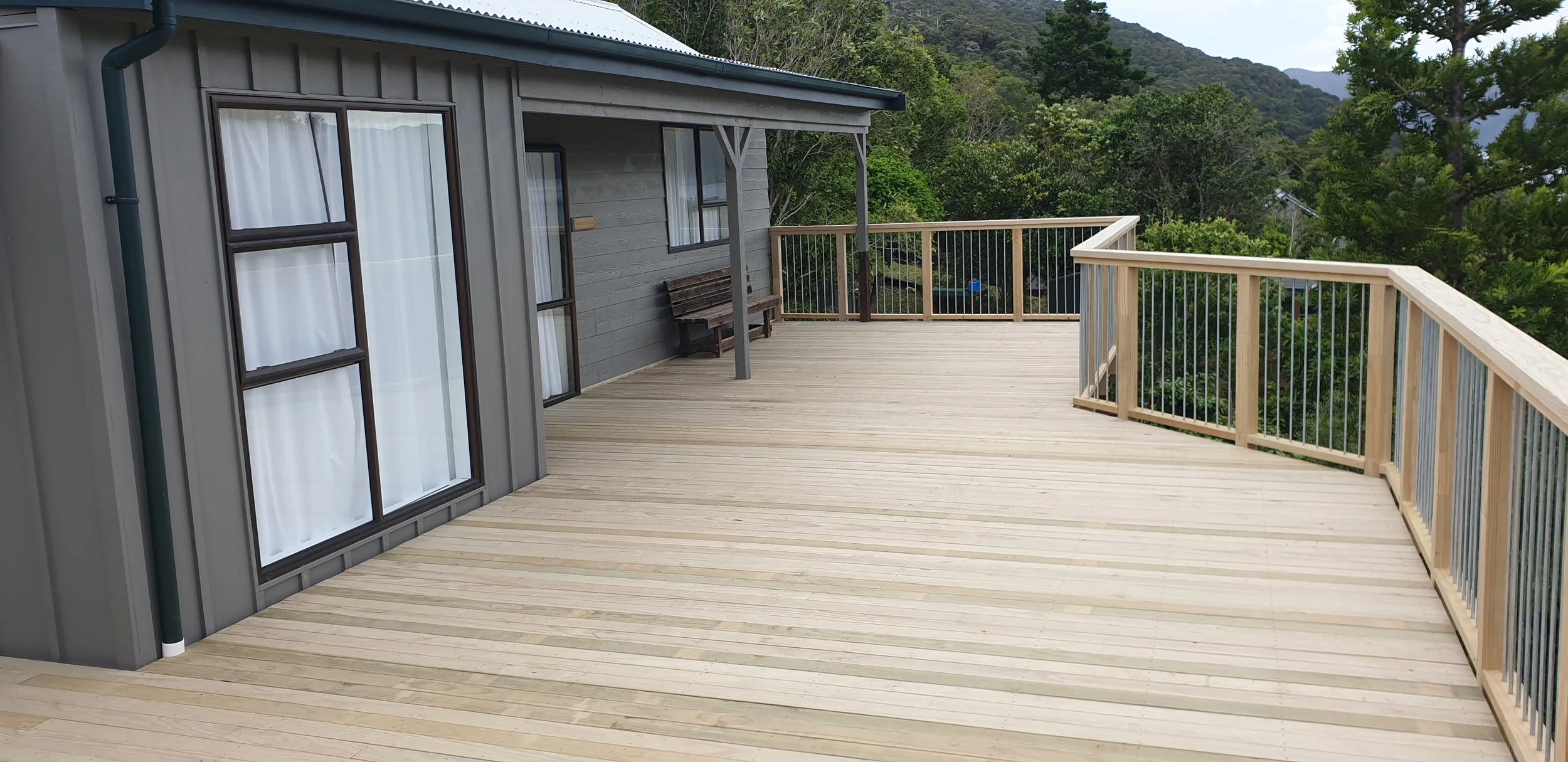 A spacious wooden balcony attached to a house, surrounded by green trees and distant mountains