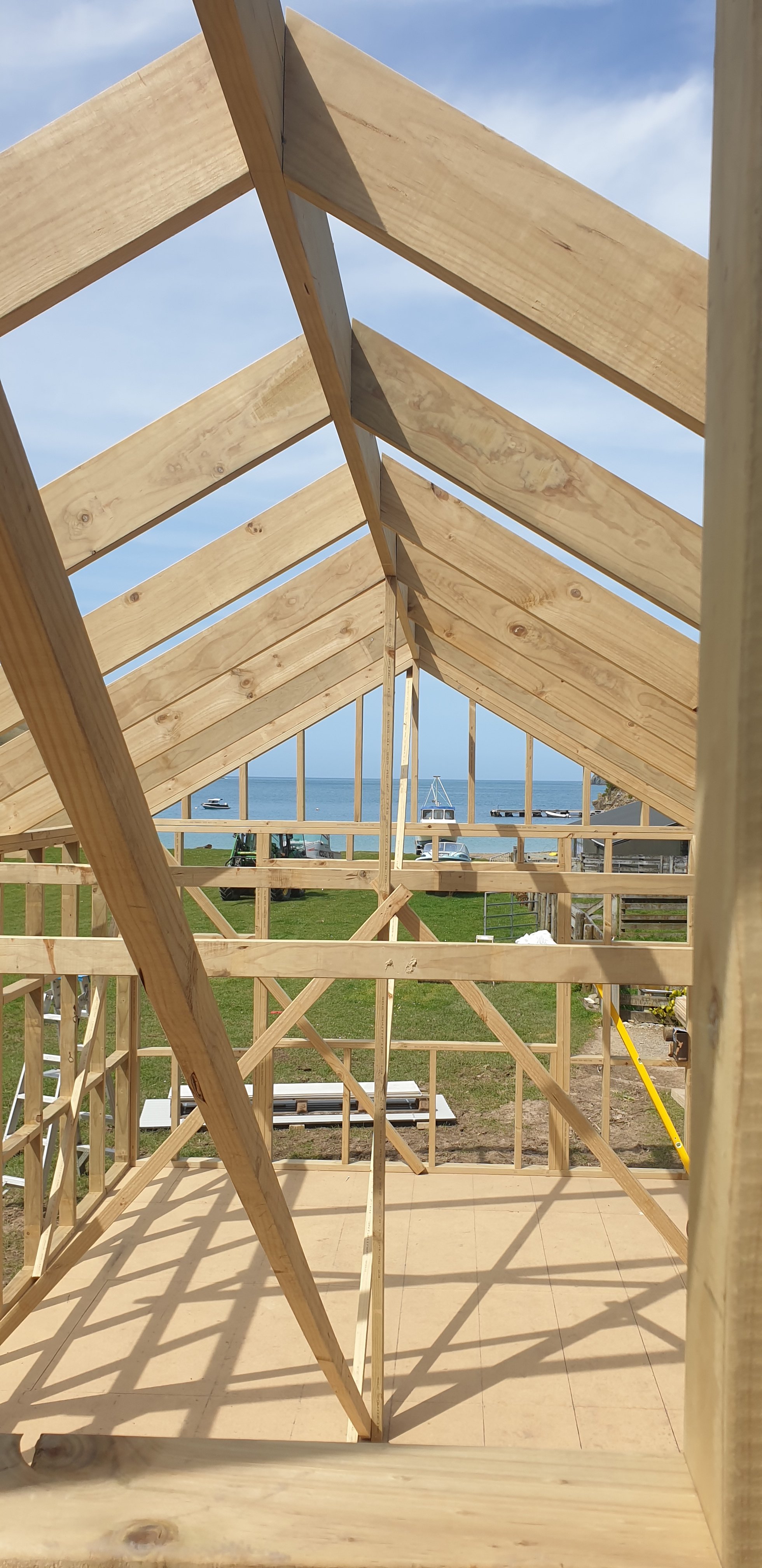View of a house under construction with a wooden frame and a view of the ocean in the background.