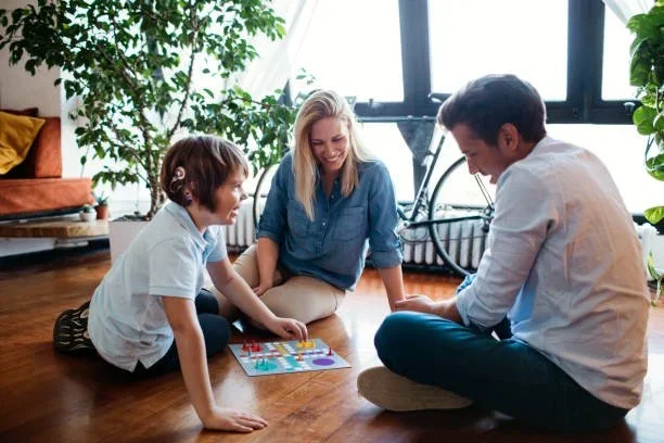 Boy with cochlear implants playing a board game with adults during Auditory Verbal Therapy session at Little Ears, Big Voices in Orange County, CA