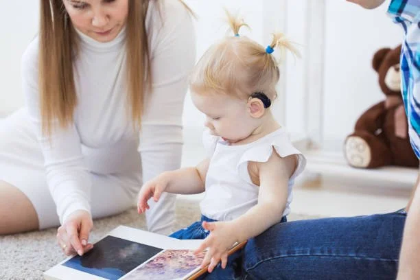 Toddler girl with hearing aids reading a book with parents during virtual Auditory Verbal Therapy session with Little Ears, Big Voices in Orange County, CA