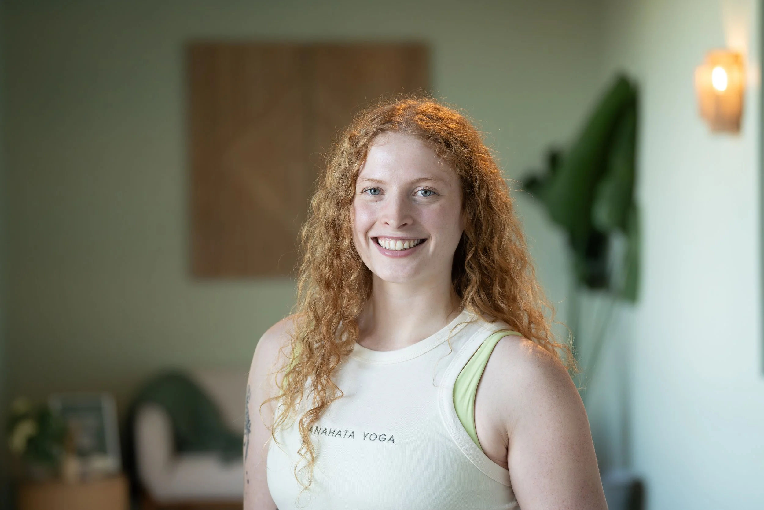 A woman with long, curly red hair, blue eyes, and fair skin smiling in an indoor setting with natural light.