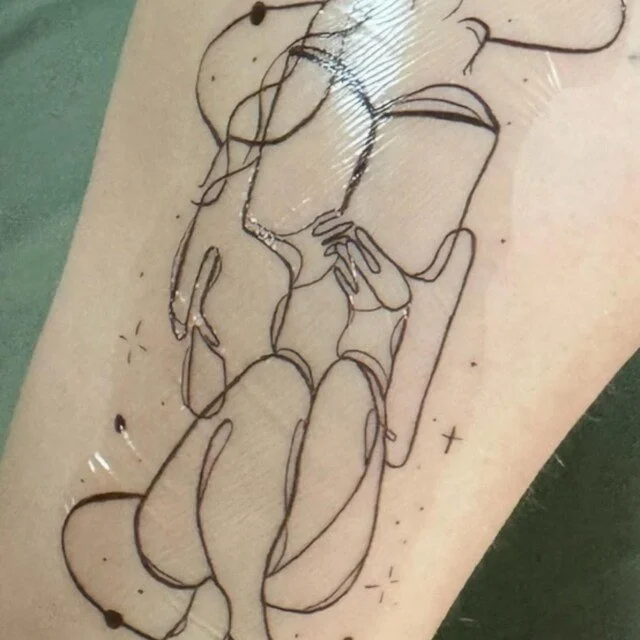 A temporary tattoo of a woman holding a coffee mug, drawn in a minimalistic, continuous line art style.