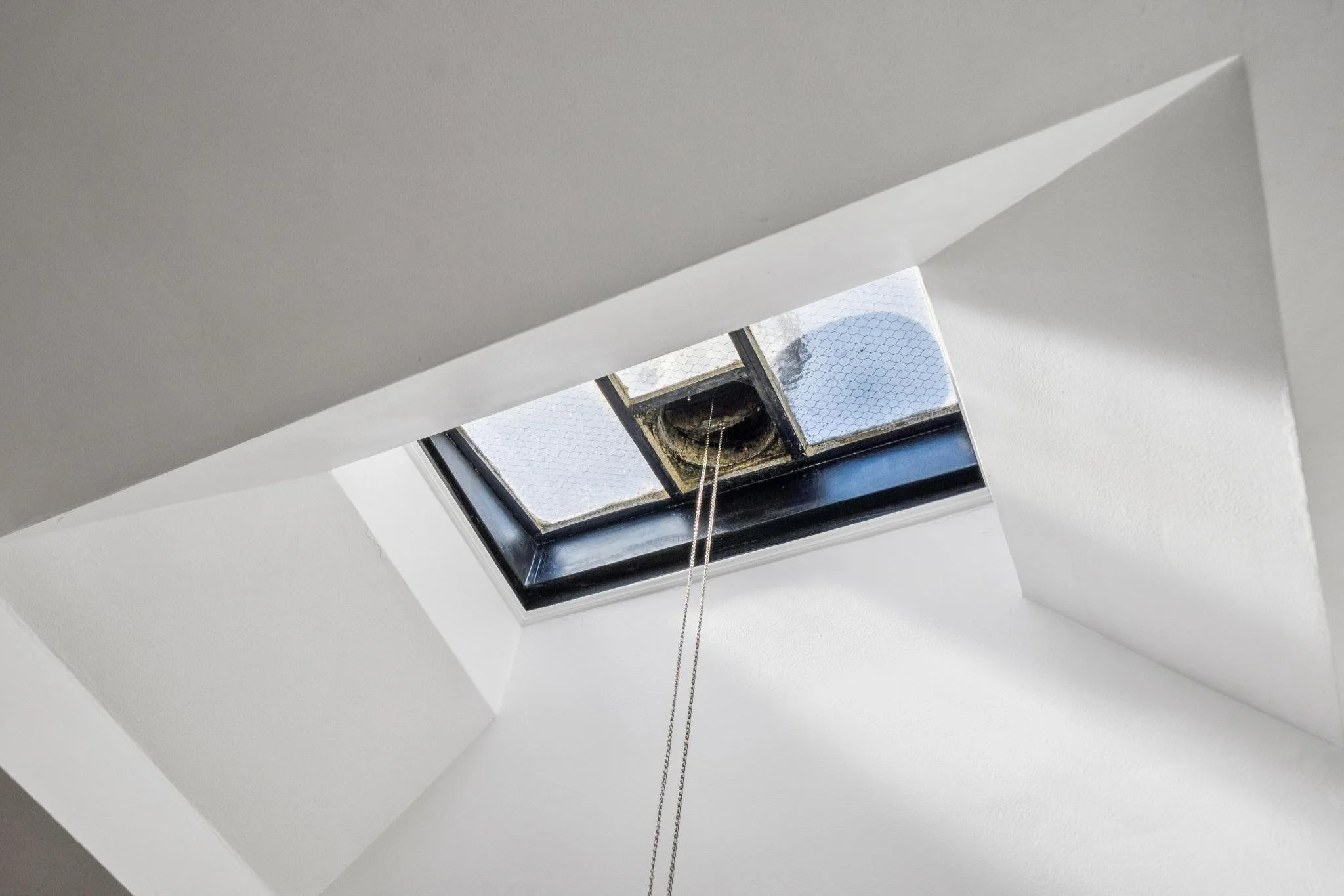 Looking up at a skylight in a white ceiling, with chains hanging down from the vent.