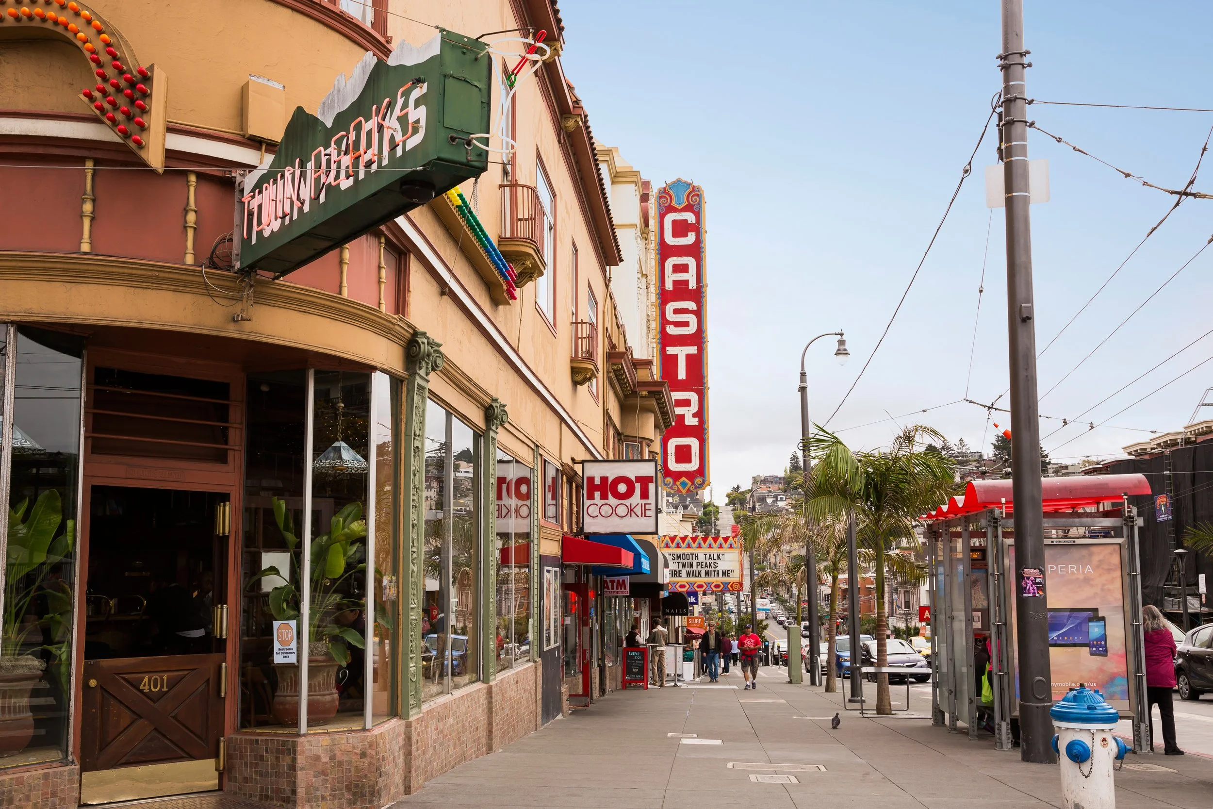 City street scene with storefronts, palm trees, and pedestrians, featuring signs for a theater, a casino, and a cookie shop.