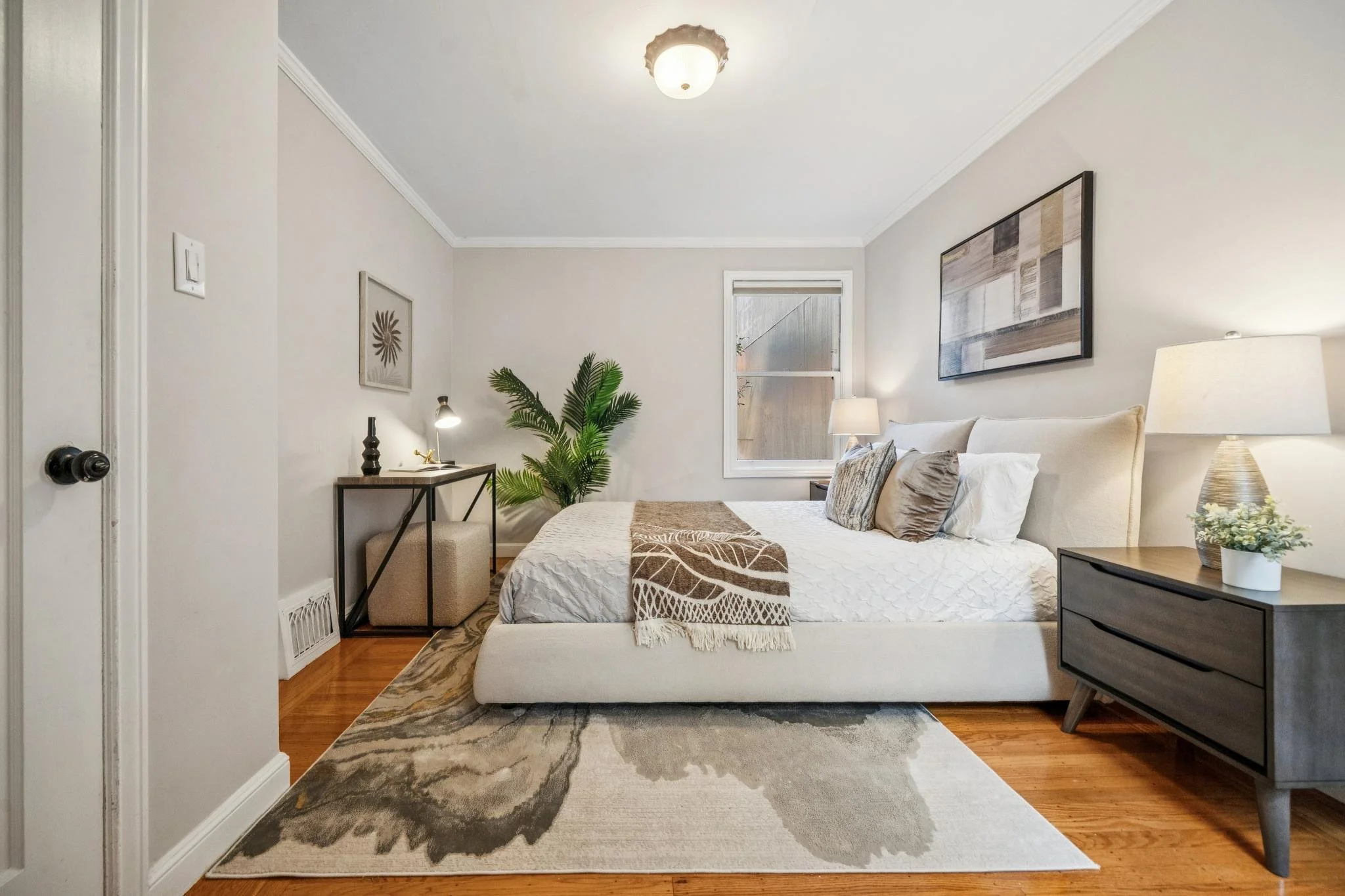 A bedroom with a bed, nightstand, and decorative plants, with minimalistic decor and soft lighting.