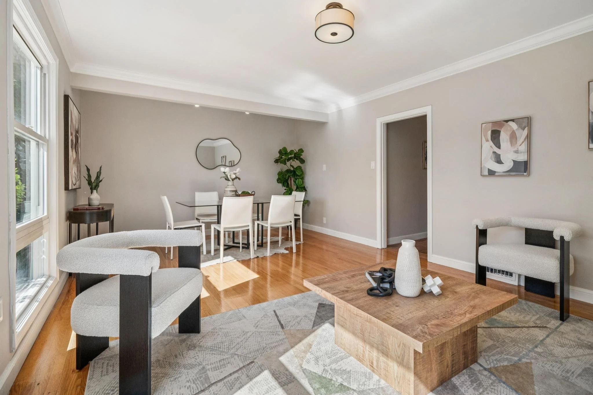 Living and dining room with large windows, wooden floors, modern furniture, wall art, and decorative items.