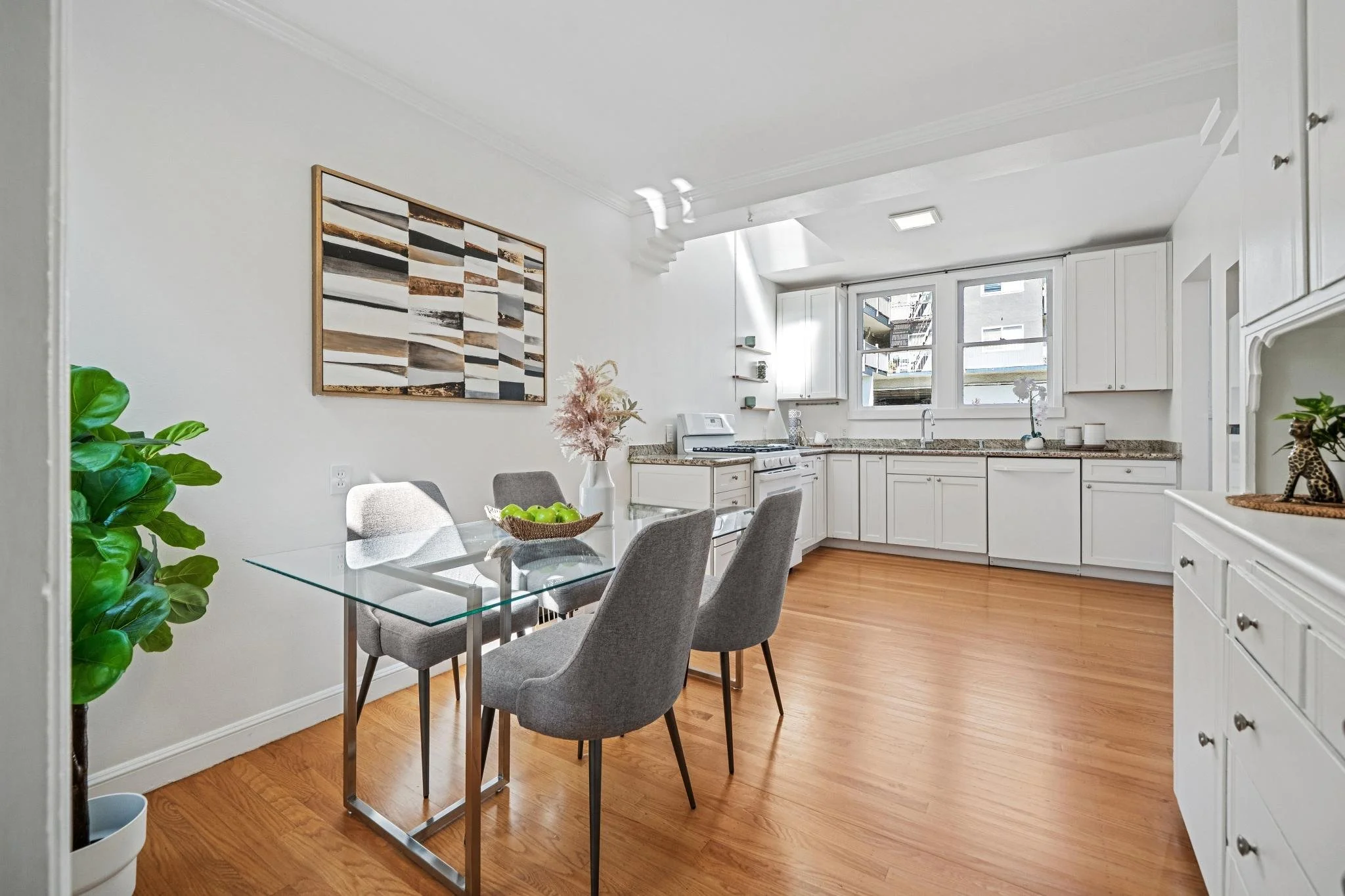 Kitchen with white cabinets, granite countertops, hardwood floor, and a dining table with four gray chairs.