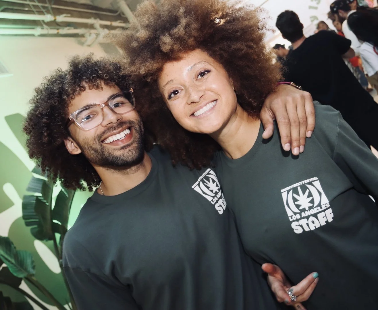 Two people smiling and posing together at an event, wearing matching green shirts with 'Los Angeles Staff' logo.