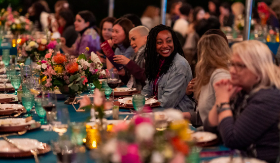 People sitting at a decorated banquet table, smiling and engaging in conversation, with colorful floral centerpieces and table settings.