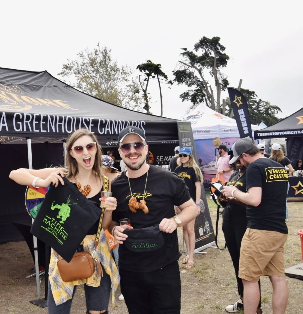 People at an outdoor cannabis festival with tents and banners, some holding drinks and wearing casual clothing.