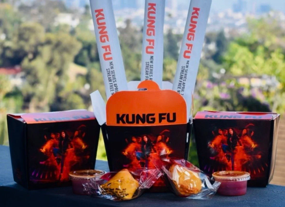 Kung Fu-themed food packages and snacks on a table outdoors, with a scenic view of trees and sky in the background.