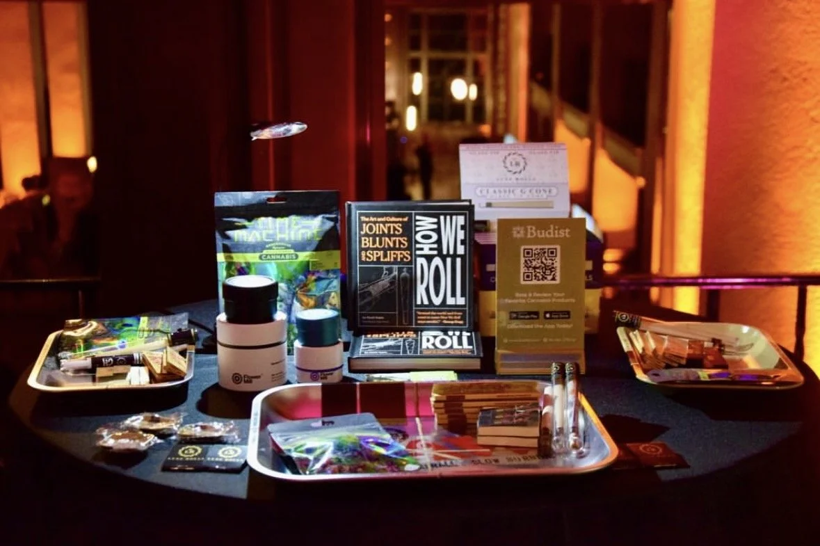 Display table with cannabis-related items, informational signs, and promotional materials in a dimly lit indoor setting.